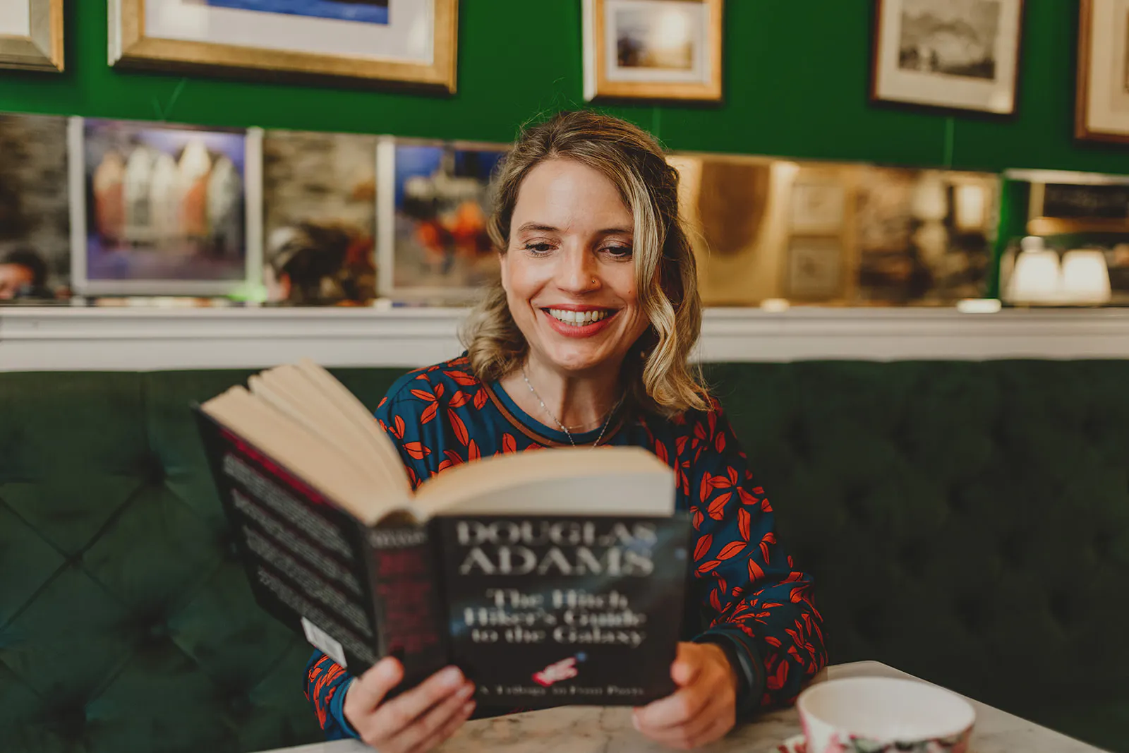 Christine Piontek sitzt in einer Teestube und liest im Sammelband von "The Hitch Hiers Guide to the Galaxy" von Douglas Adams.