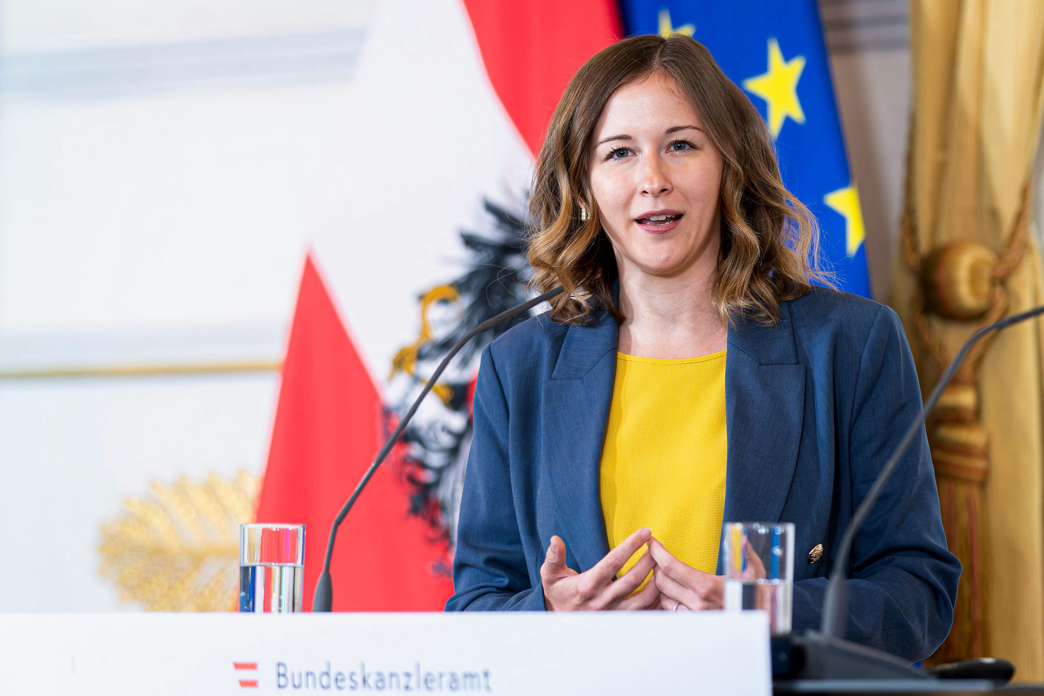Claudia Plakolm, Integrationsministerin der ÖVP, spricht bei einer Pressekonferenz im Bundeskanzleramt. Sie steht vor einem Rednerpult. Hinter ihr sind die österreichische und die EU-Flagge zu sehen.