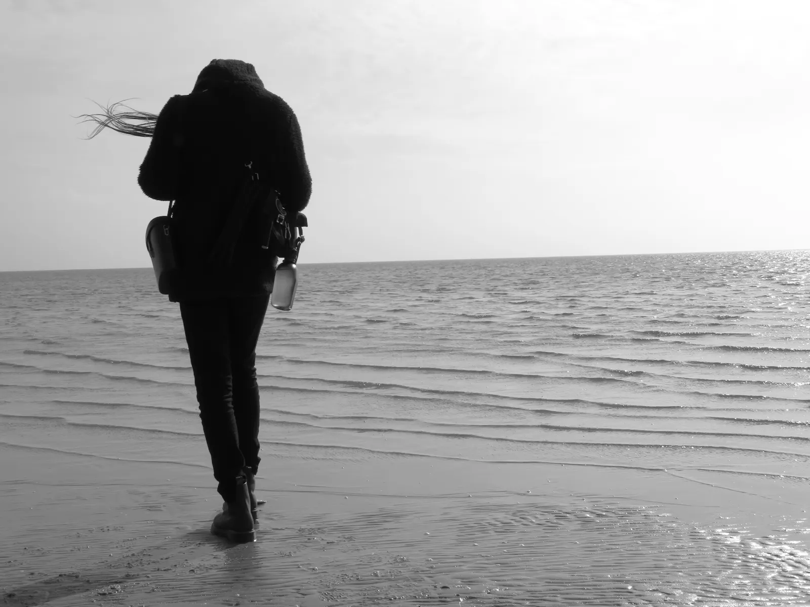 Schwarz-weiße Fotografie. Eine schlanke Person steht am Meeresufer.