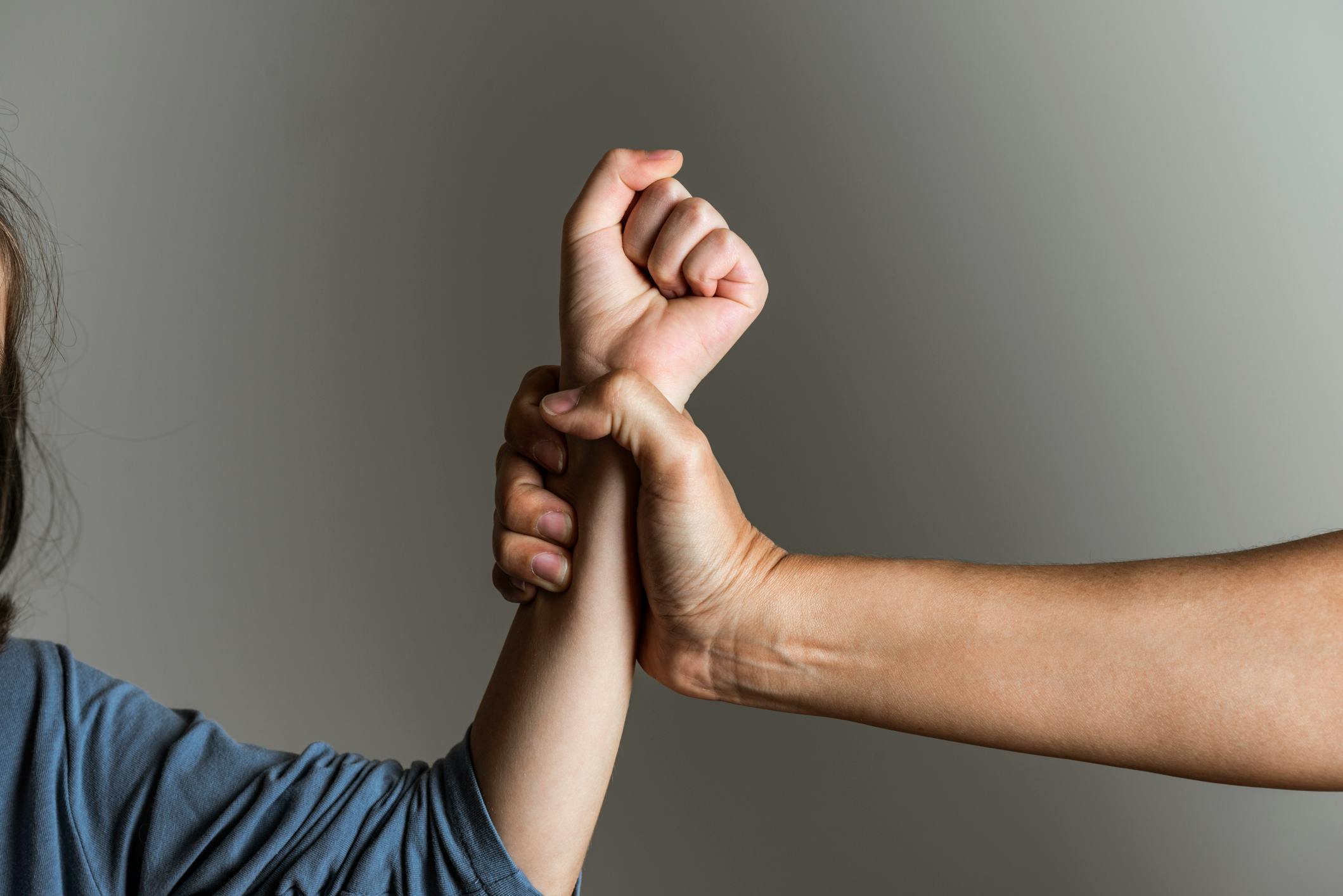 Dieses Foto zeigt symbolisch Gewalt gegen ein Kind: Eine erwachsene Hand greift fest nach dem Arm eines Kindes, das sich zu schützen versucht.