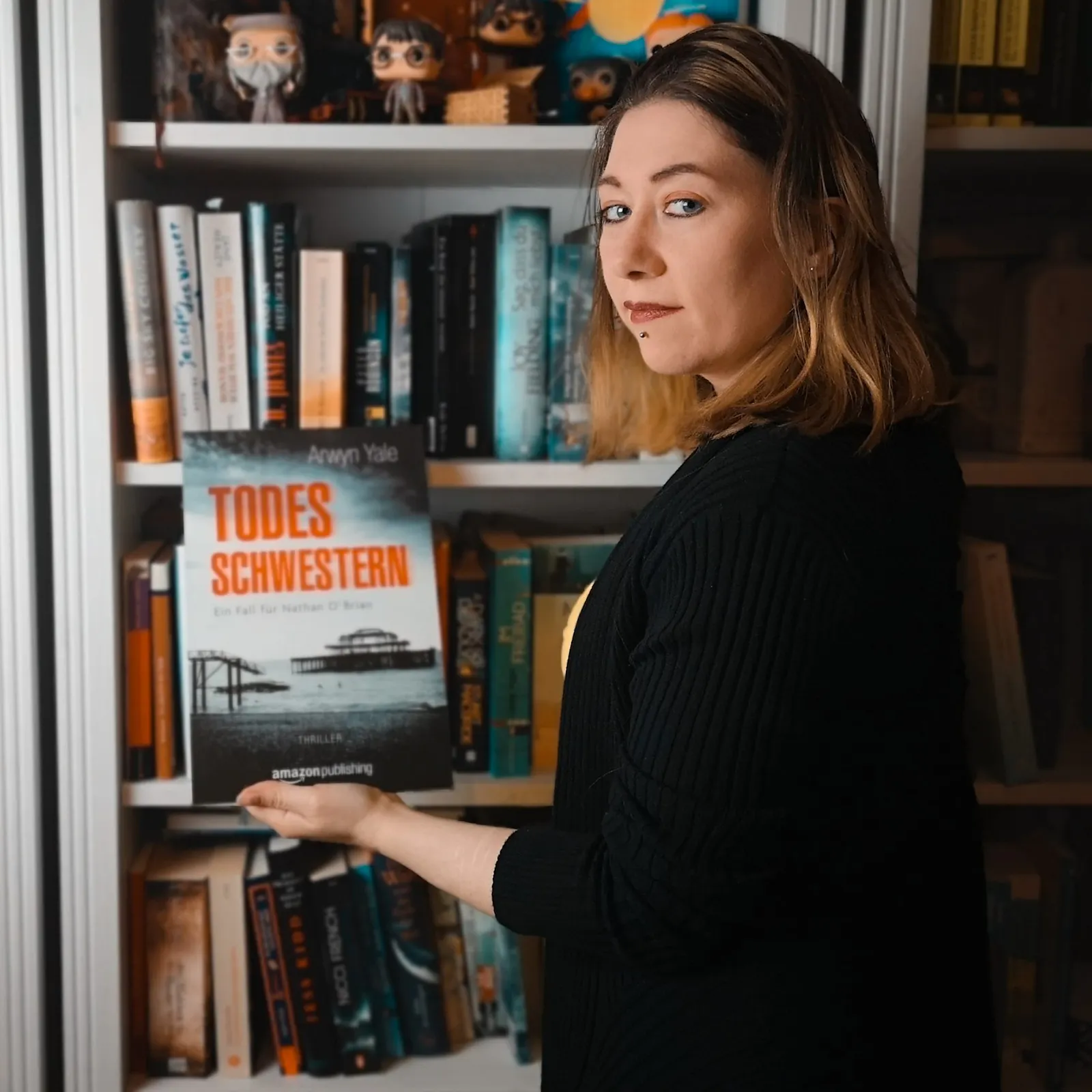 Arwyn Yale vor einem Bücherregal hält ein Cover von ihrem Thriller Todesschwestern in der Hand