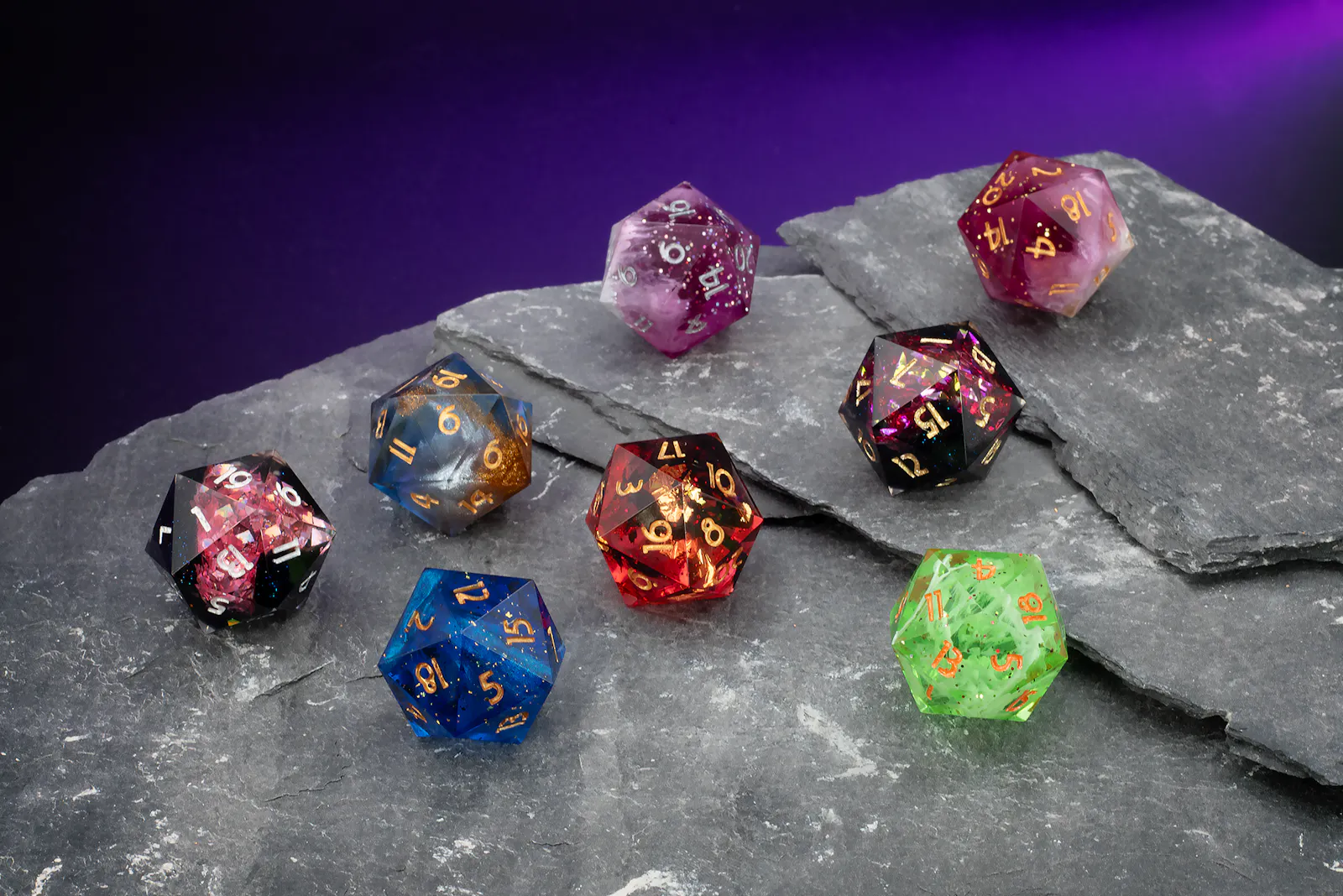 Verschiedene D20-Würfelsets in Blau, Rot, Grün, Lila und Schwarz mit goldenen, weißen und silbernen Zahlen, dekorativ auf einer Schieferplatte präsentiert.