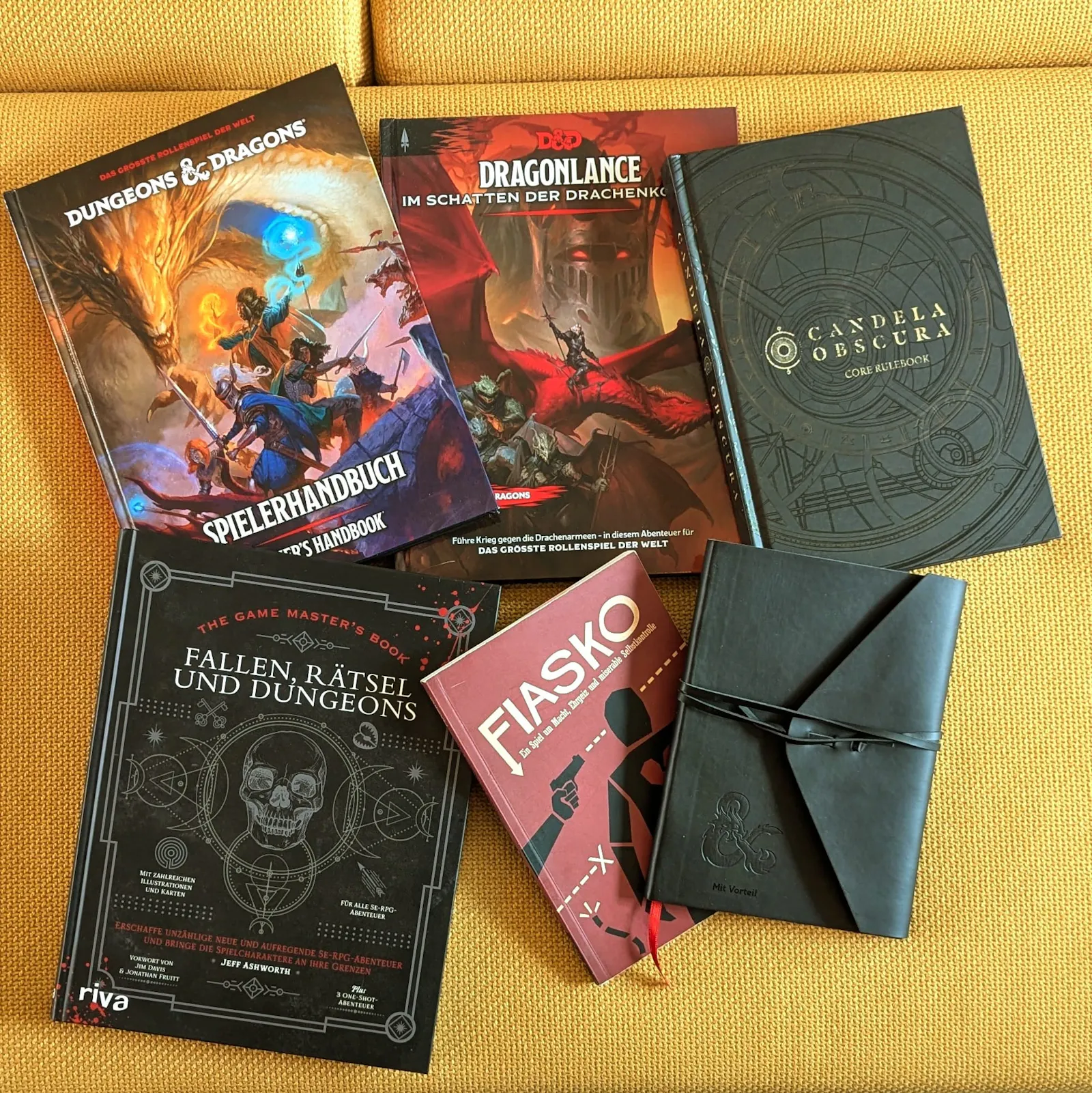 Ein Foto mit dem Preispool für den Mach ein Monster Wettbewerb! Zu sehen sind die Bücher Players Handbook 2024 auf Deutsch, Dragonlance Deutsch, Candela Obscura, Fiasko Deutsch, Fallen, Rätsel und Dungeons und ein hübsches Notizbuch mit "Mit Vorteil" Gravur.