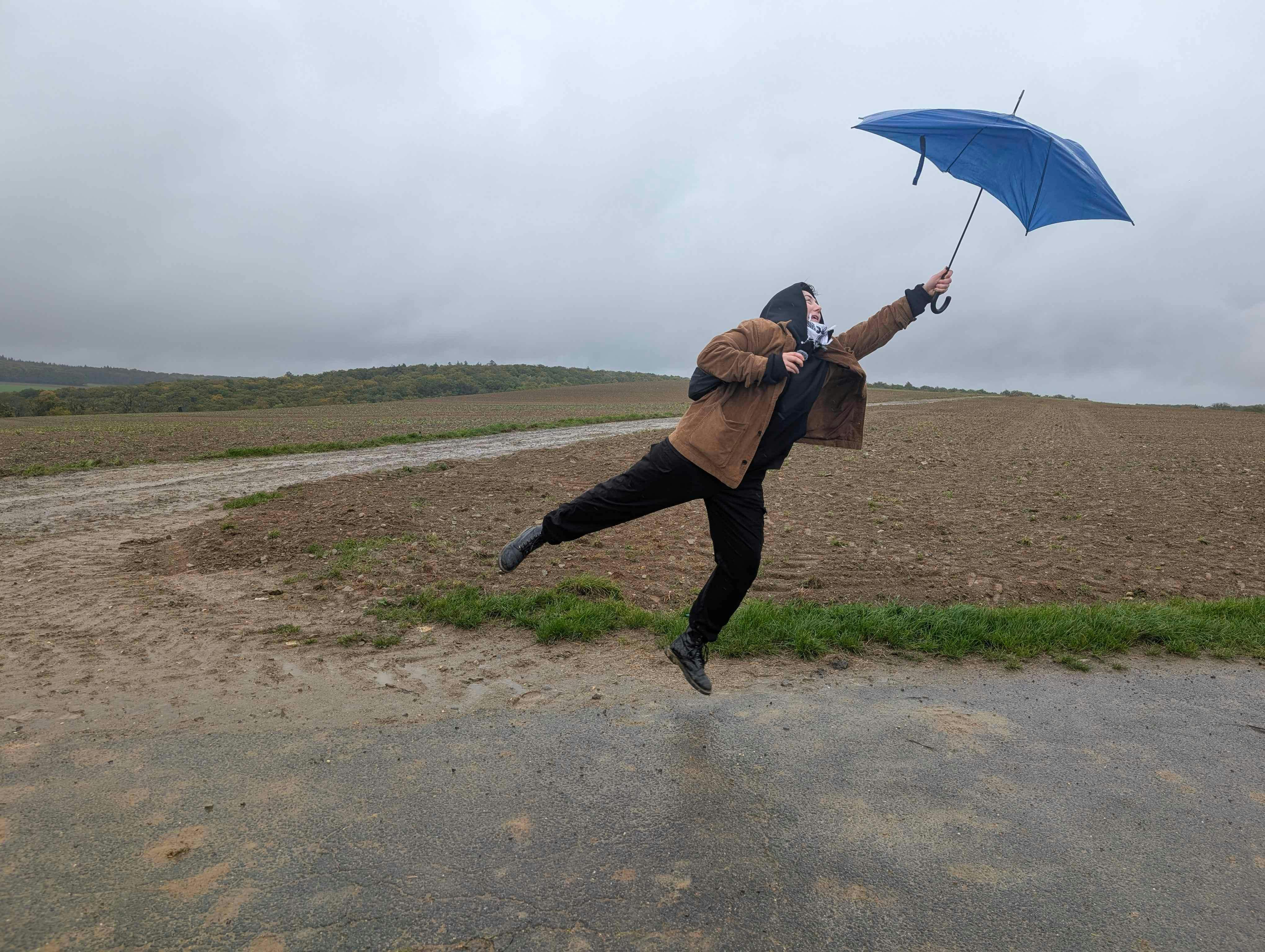 Tryn hält sich an einem Regenschirm fest und wird vom Winde verweht.