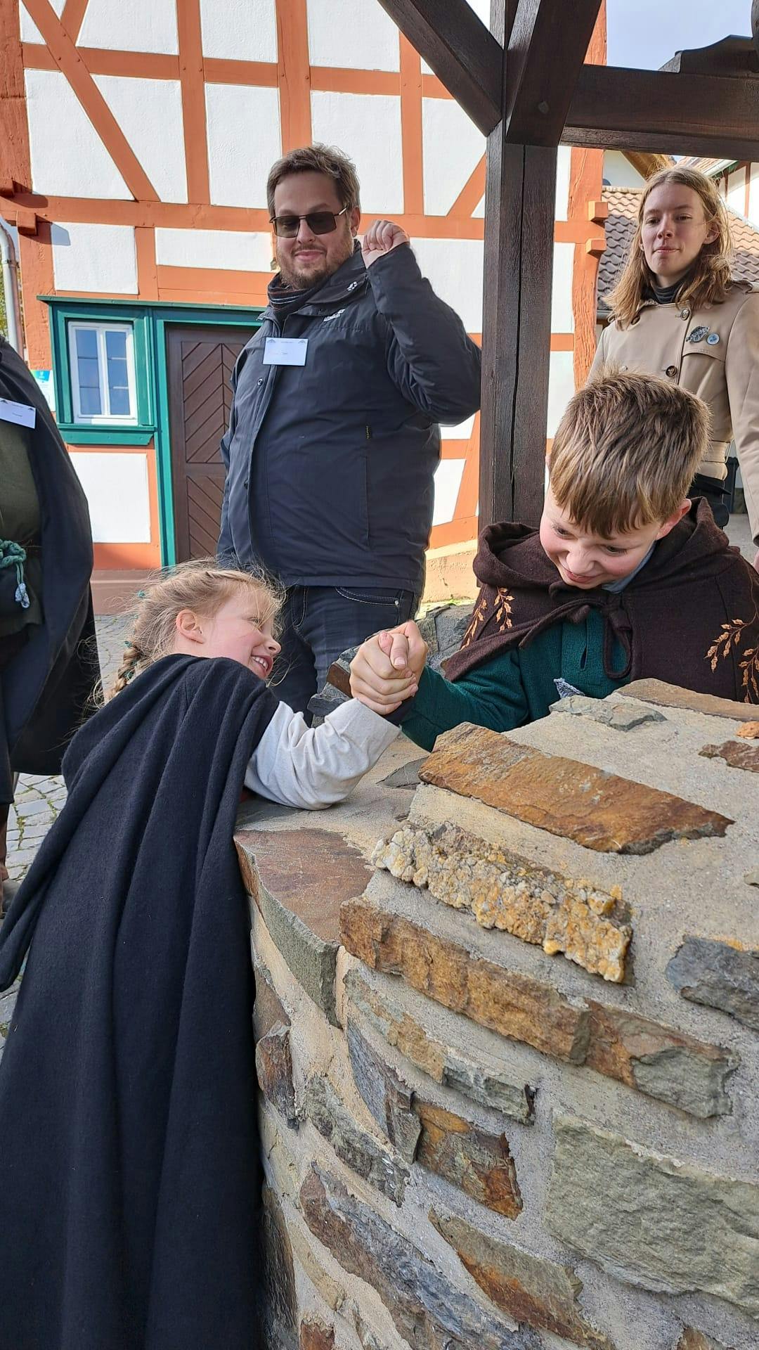 Zwei Kinder machen Armdrücken, um herauszufinden, wer stärker ist und werden dabei von zwei Erwachsenen angefeuert.