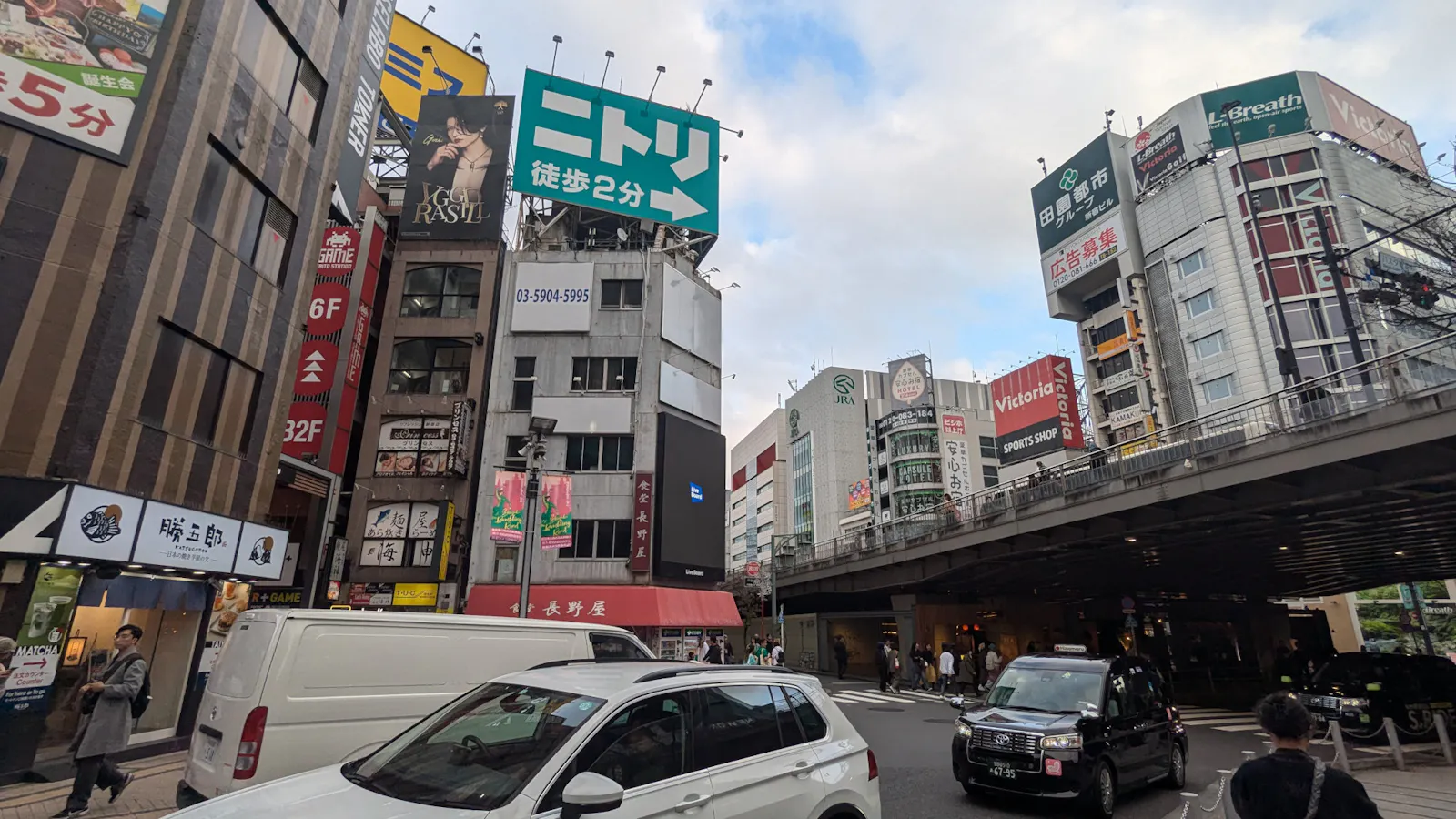 Straßenkreuzung in Shinjuku, Tokio. Straße, Hochbahn, Häuser, Autos.