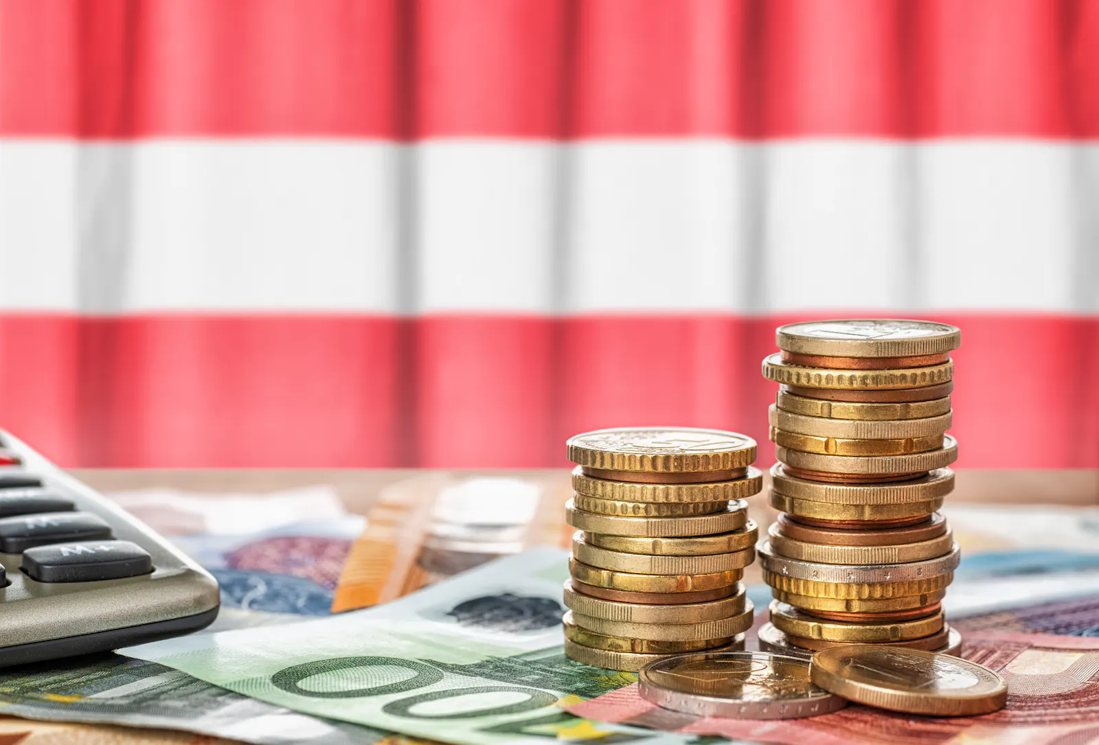 Das Bild zeigt Euro-Münzen und Euro-Scheine vor einer österreichischen Flagge sowie einen Taschenrechner.