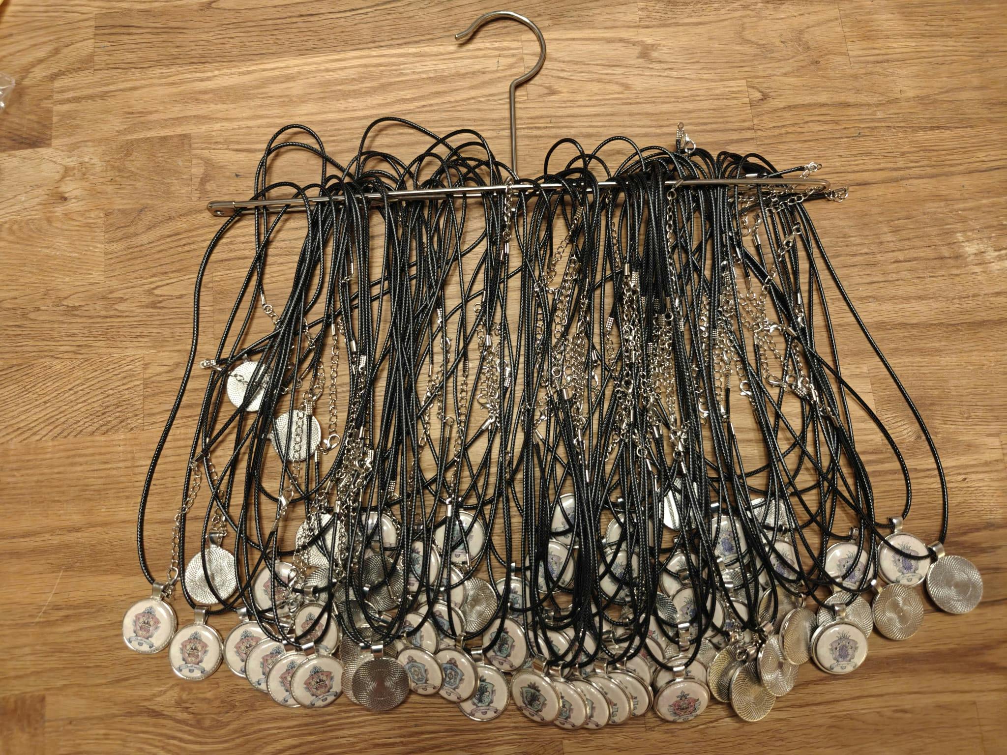 Ein Bügel, an dem zahlreiche Amulette an schwarzen Kordeln hängen. Jedes Amulett ist ein runder Anhänger mit silbernem Rand, der ein Thaya-Reichswappen zeigt.