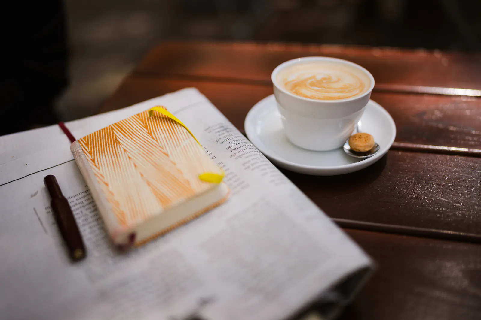 Gefüllte Kaffeetasse, Notizbuch und Zeitung auf einem Tisch.