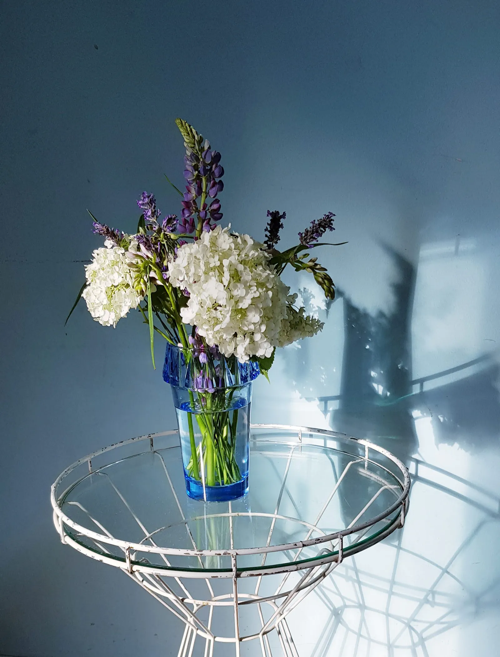 Gartenstrauß in hellblauer Kristallvase mit weißen Hortensien und violetten Lupinen