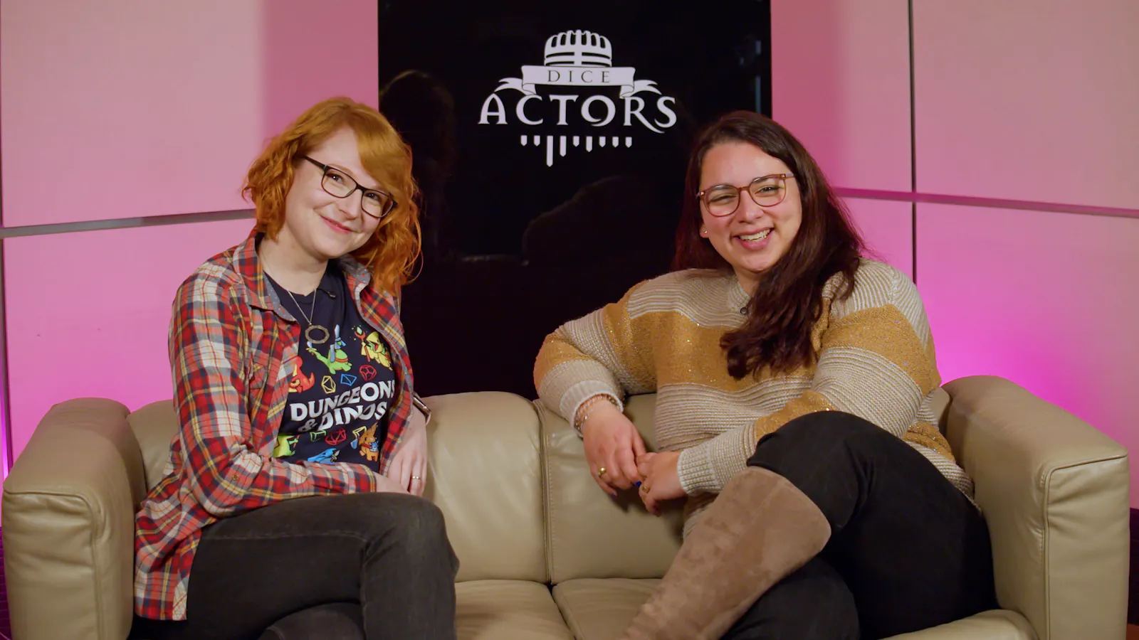 Stephie und Aylin sitzen glücklich auf einem Sofa, dahinter steht "Dice Actors" auf einer schwarzen Glasplatte.