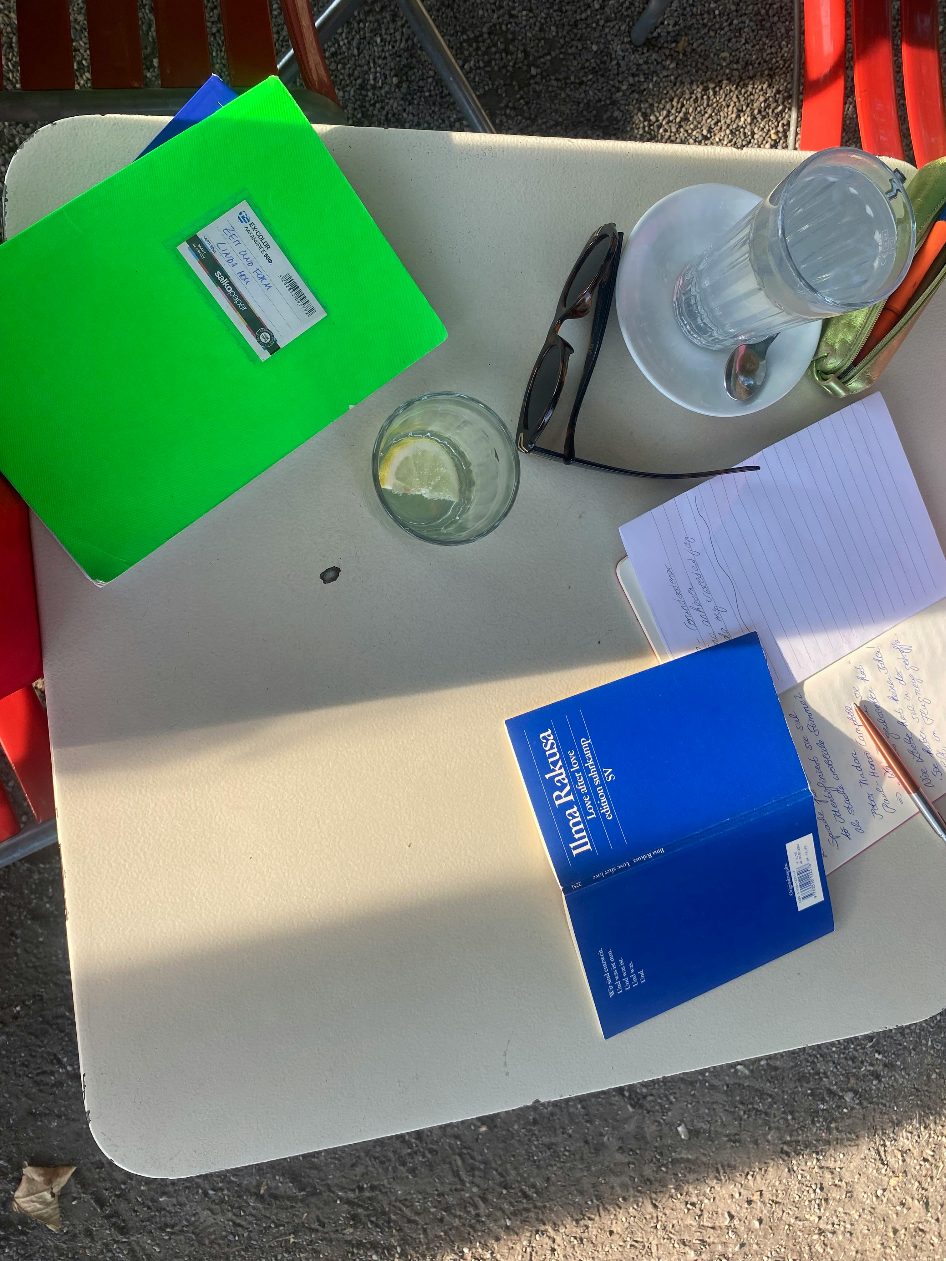 Ein Arbeitsplatz im Freien mit einem Notizbuch und dem Buch "Love after Love" von Ilma Rakusa.