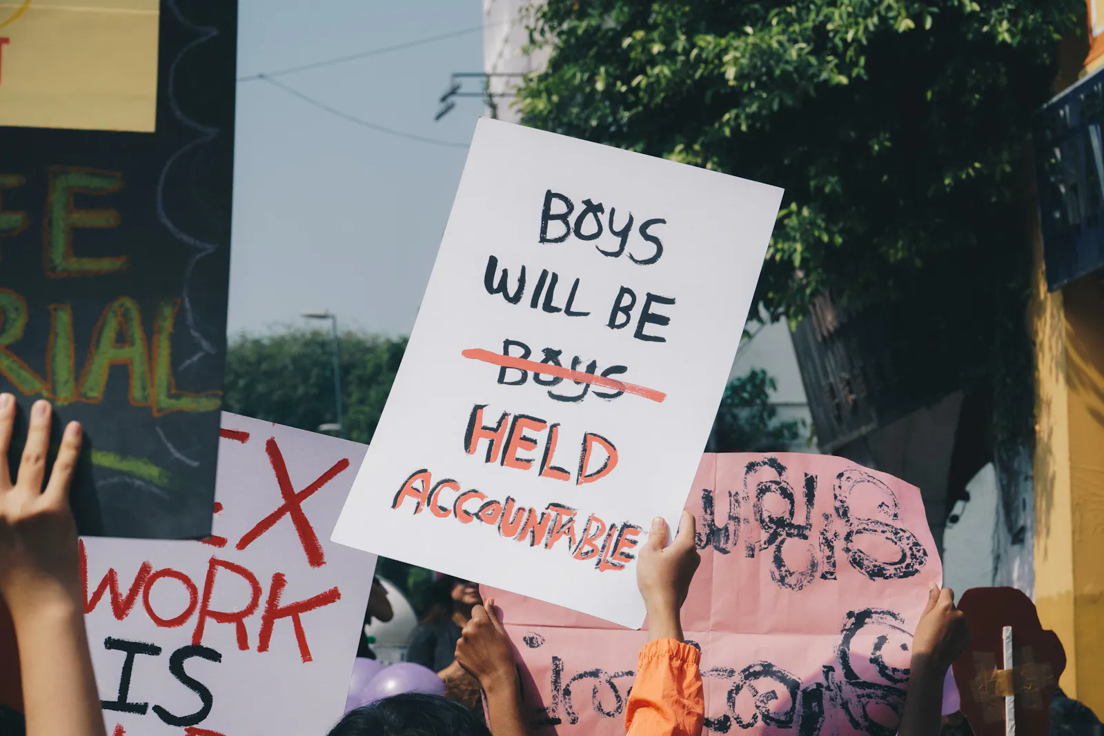 Demo-Szene: Ein Schild wird hochgehalten auf dem steht: "Boys will be boys", "boys" ist durchgestrichen und durch "held accountable" ersetzt.