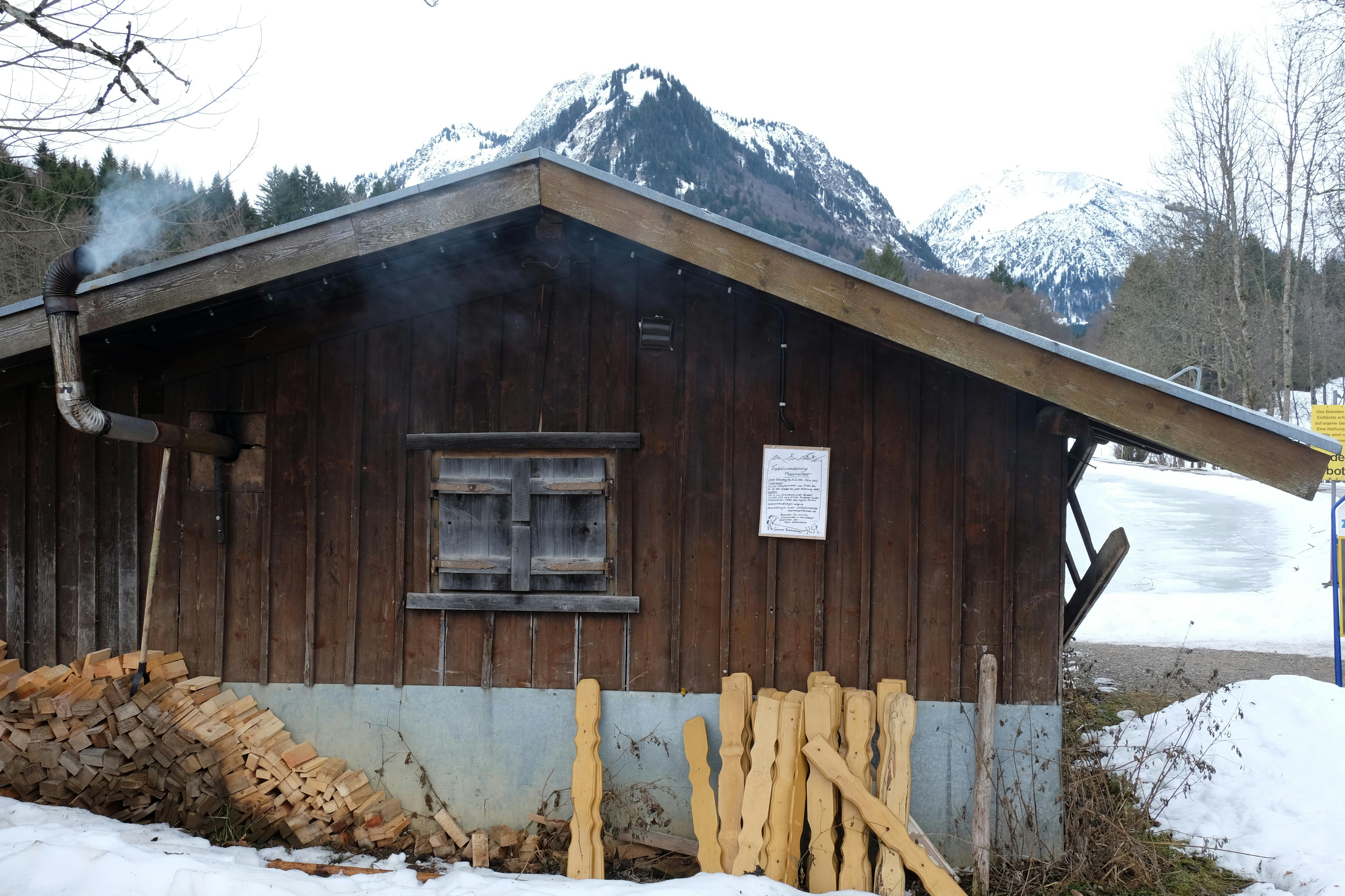 Hütte in den Bergen, aus deren Schornstein es raucht. Vor der Hütte liegt Holz für den Ofen.
