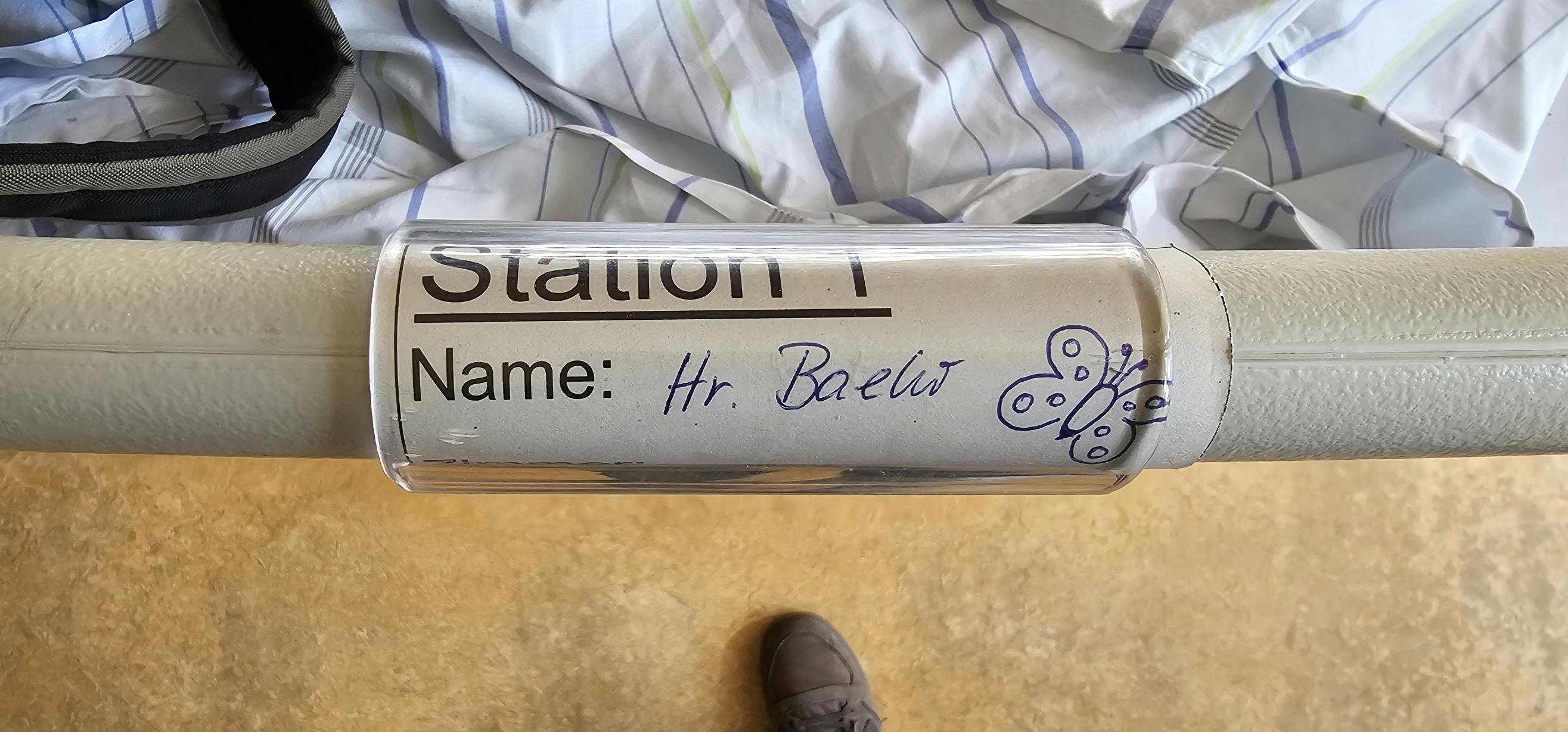 Ein Teil des Bettgestells im Krankenhaus, auf dem "Station 1, Name: Hr. Baehr" steht und ein Schmetterling gemalt ist.