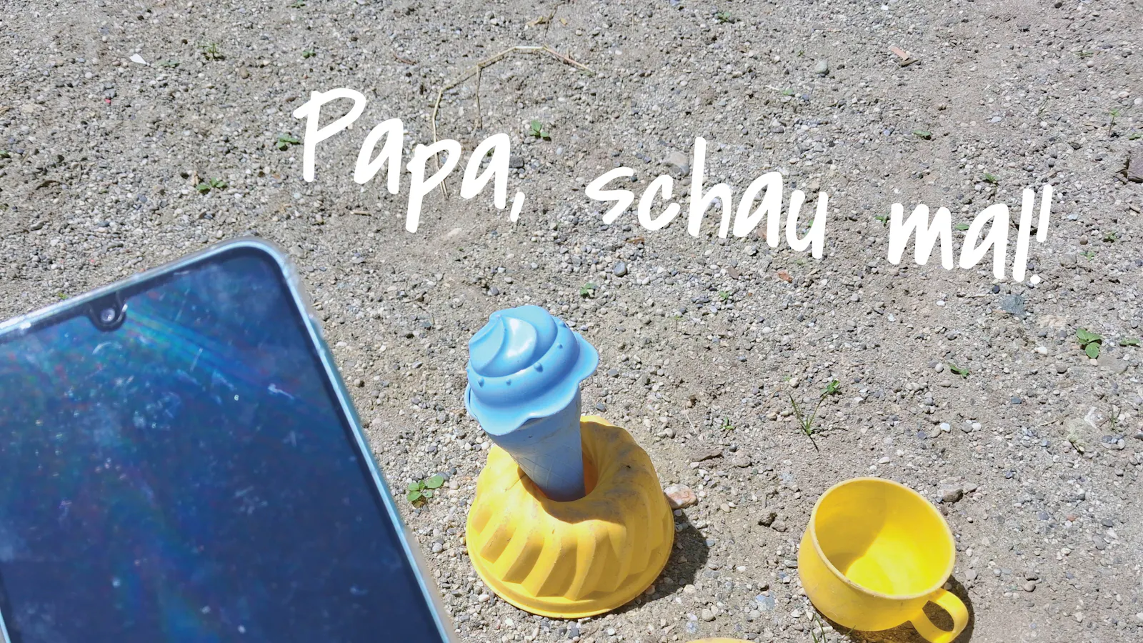 Spielzeug im Sandkasten, im Vordergrund ein Handy