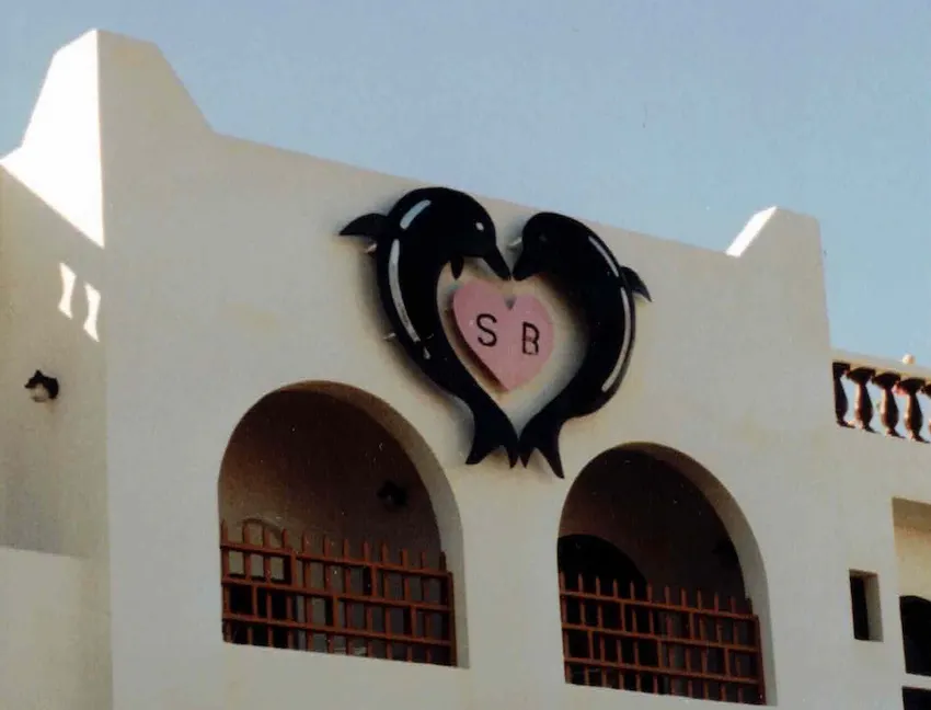 Fassade eines Hotels in Griechenland mit zwei Delfinen, die ein Herz bilden, zwischen ihnen ein rosa Herz mit den Buchstaben SB