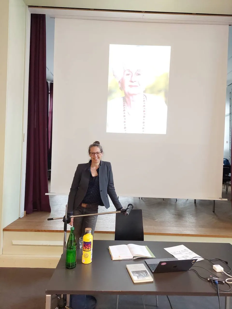 Foto: Tanja Mohr/
Corinna Below steht vor der Leinwand, auf dem ein Foto einer der EIN STÜCK DEUTSCHLAND Protagonistinnen zu sehen ist. Im Vordergrund ein Tisch mit Laptop und Buch.