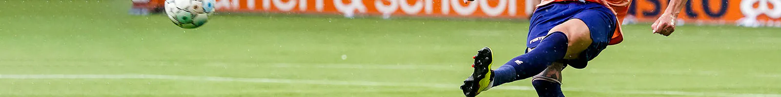 Auf einem Fußballfeld schießt ein Fußballer einen Ball in die Luft.