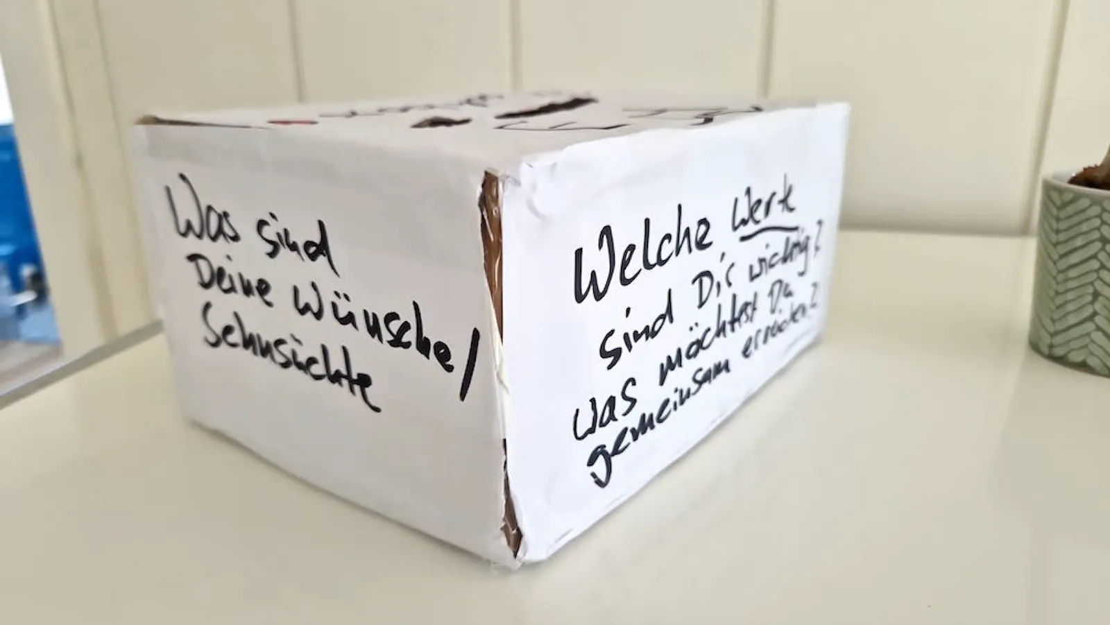Das Bild zeigt eine Kiste mit Schlitz oben und Sprüchen an der Seite: "Was sind deine Wünsche oder Sehnsüchte?"