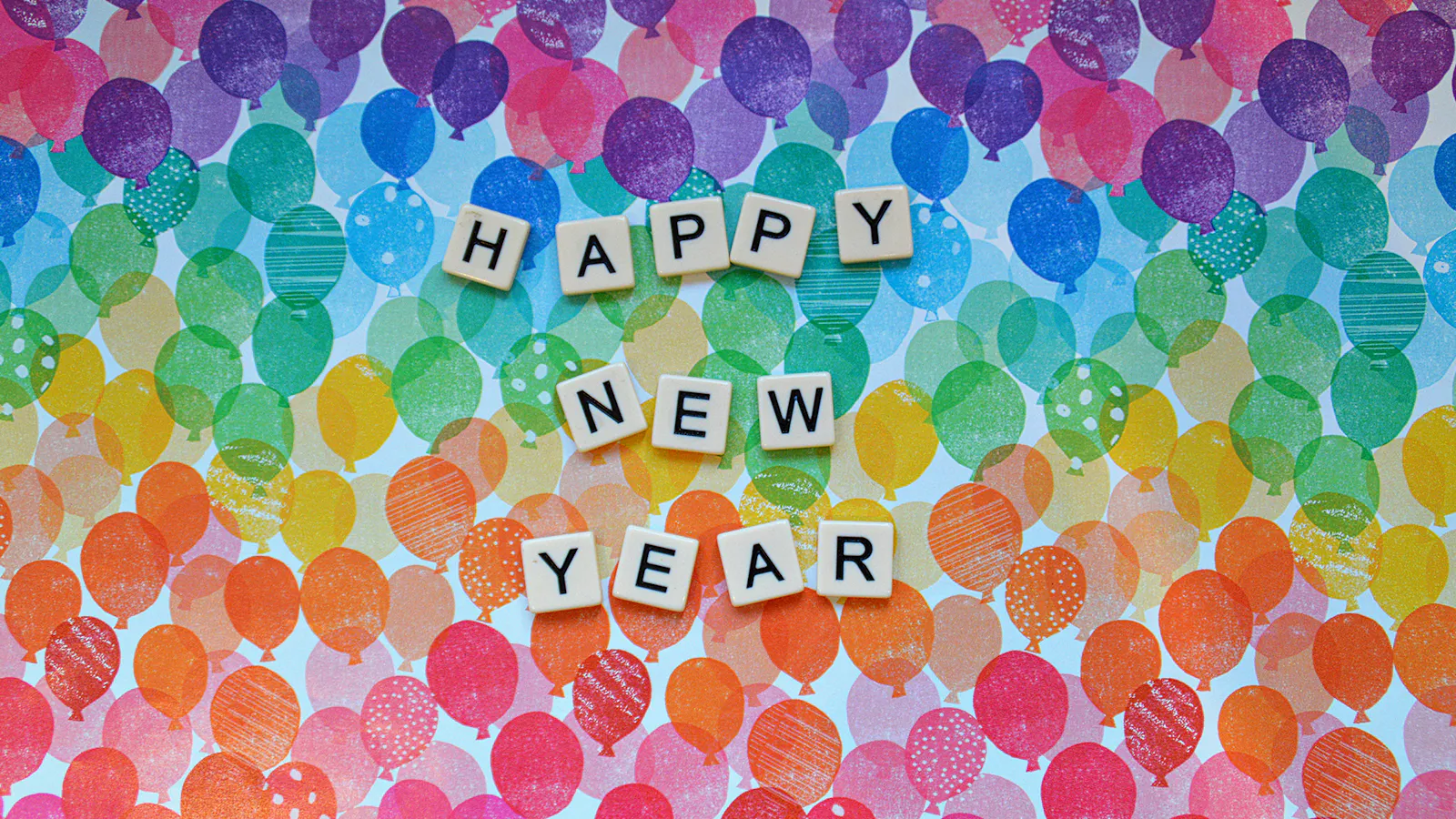 Bausteine mit Buchstaben bilden die Worte "Happy New Year" vor einem Hintergrund aus bunten Ballon-Stempelmotiven