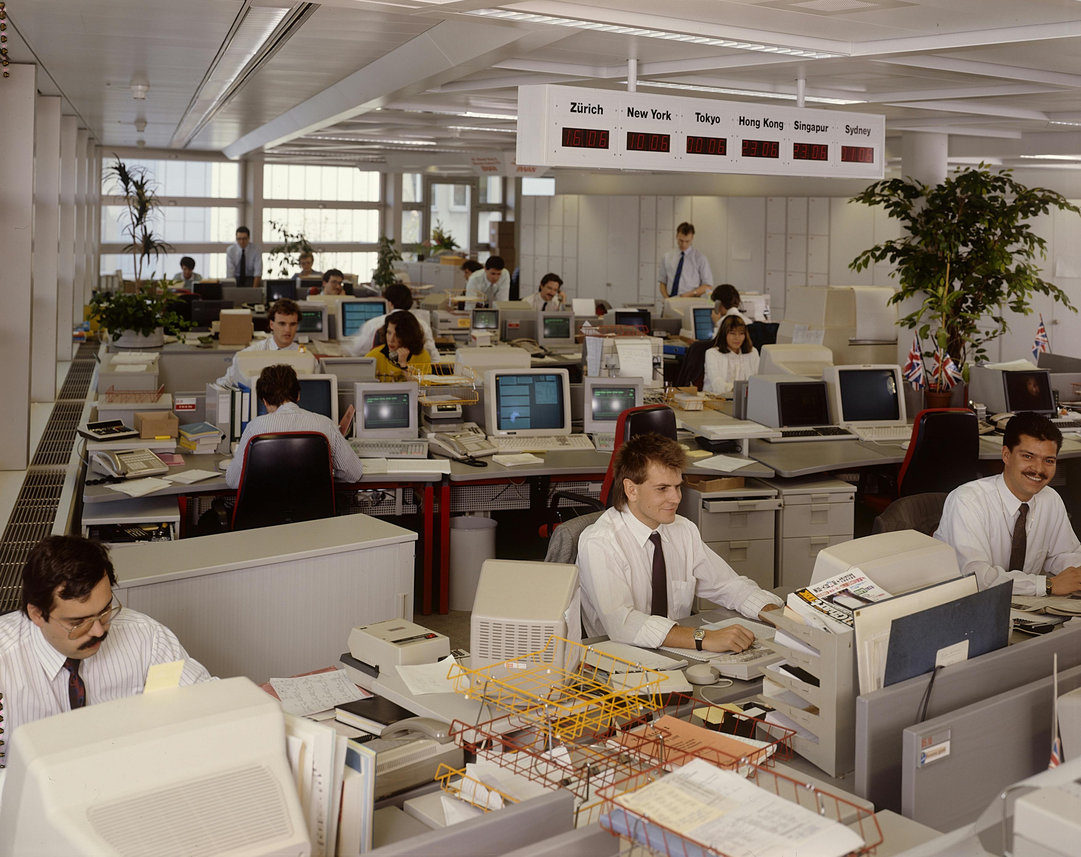 Blick in ein Grossraumbüro, ganz viele alte Computer mit Röhrenmonitoren. Die Angestellten sitzen an ihren Arbeitsplätzen.