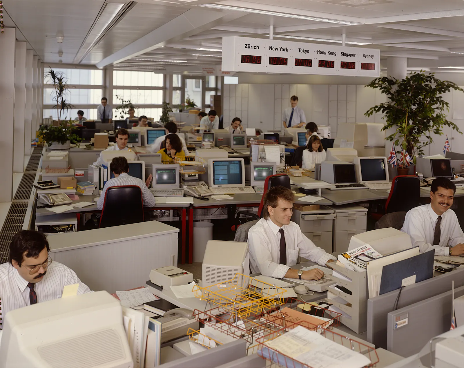 Blick in ein Grossraumbüro, ganz viele alte Computer mit Röhrenmonitoren. Die Angestellten sitzen an ihren Arbeitsplätzen.