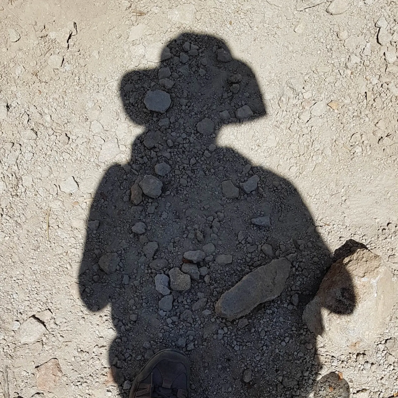 Der Schatten einer Person mit Hut auf grauem Geröll