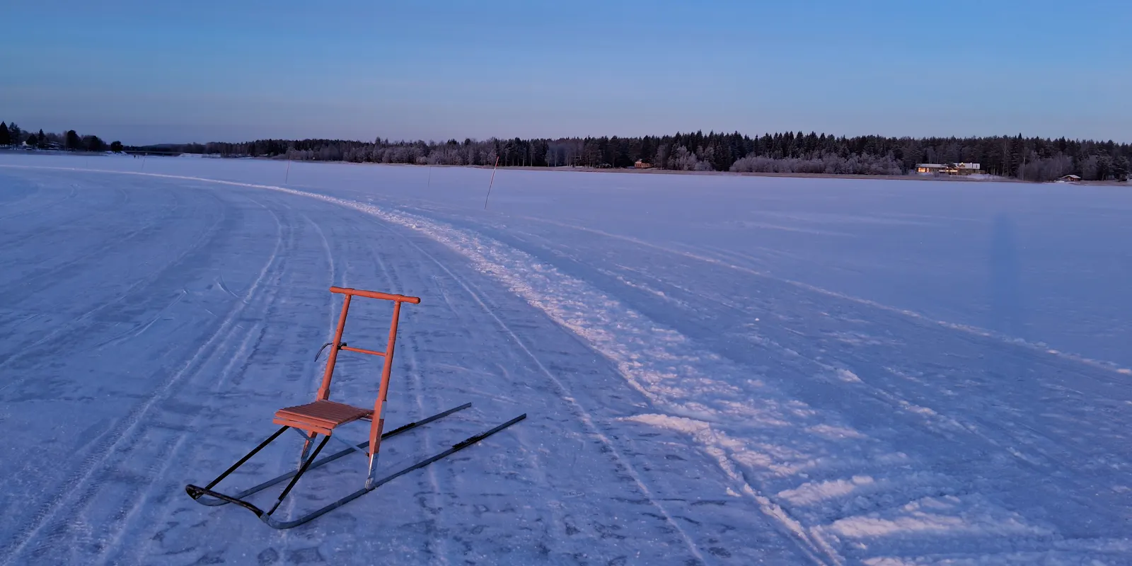 Oranger Tretschlitten, verschneite Eisfläche, am Horizont Land