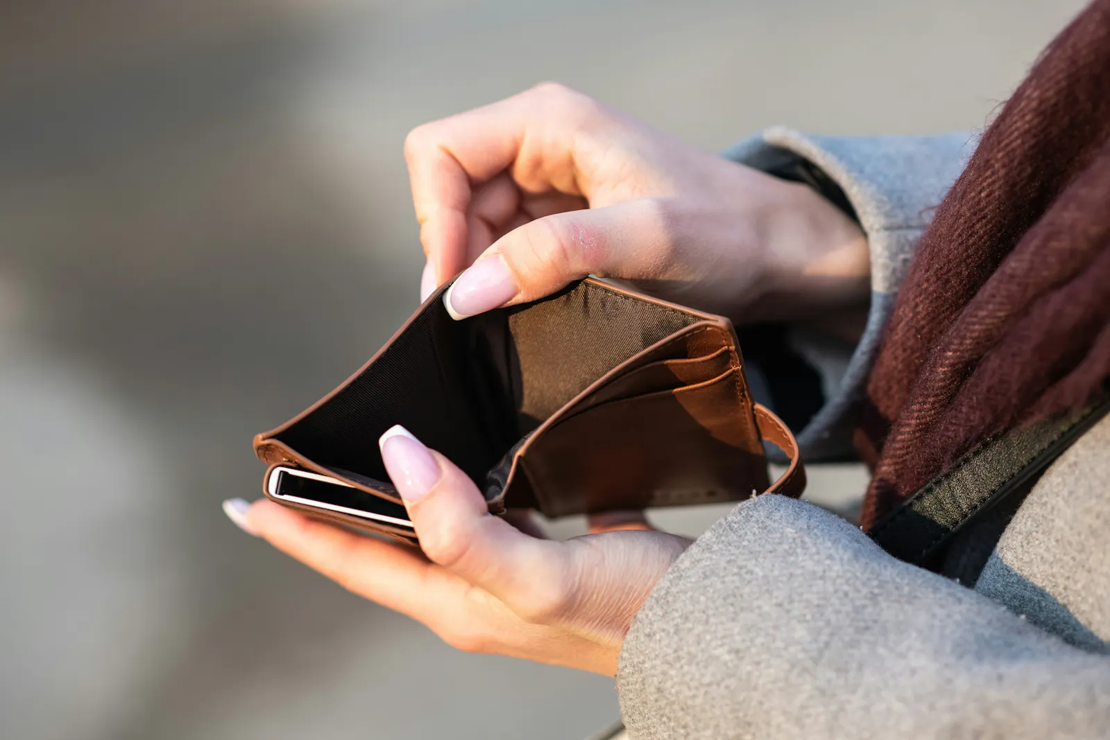 Eine Person hält ein braune lederne Geldbörse in den Händen. Die Geldbörse ist aufgefächert und leer.