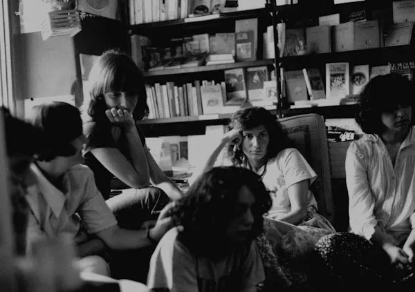Schwarz-Weiß-Foto einer Gruppe diskutierender Frauen vor einem Bücherregal.