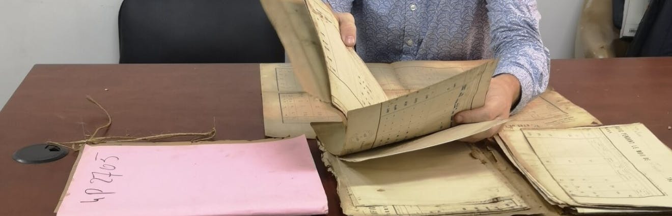 Person hält vergilbte Archivalien auf einem Schreibtisch in der Hand