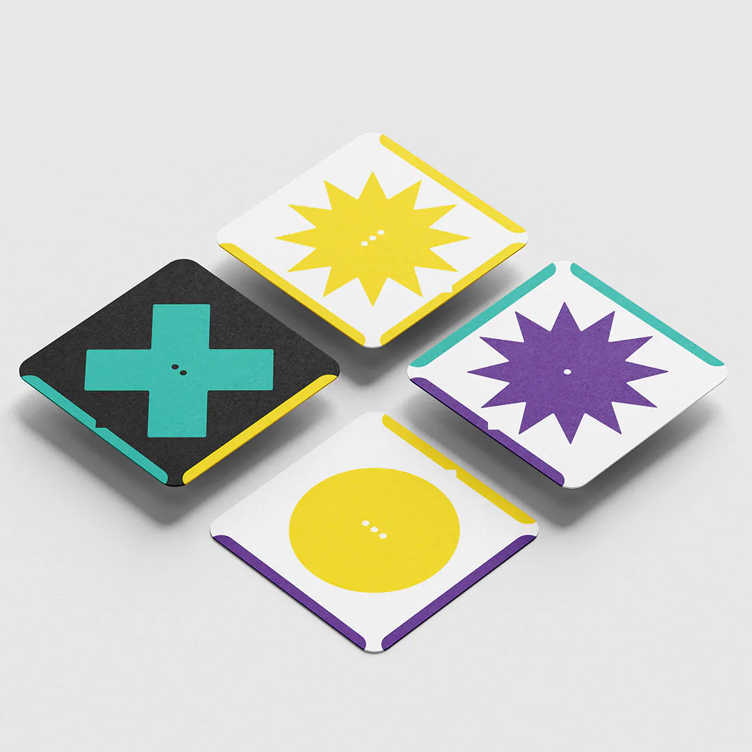 Four square cards with geometric shapes including a teal cross on black, a yellow starburst on white, a purple starburst on white, and a yellow circle on white, each with colored edges