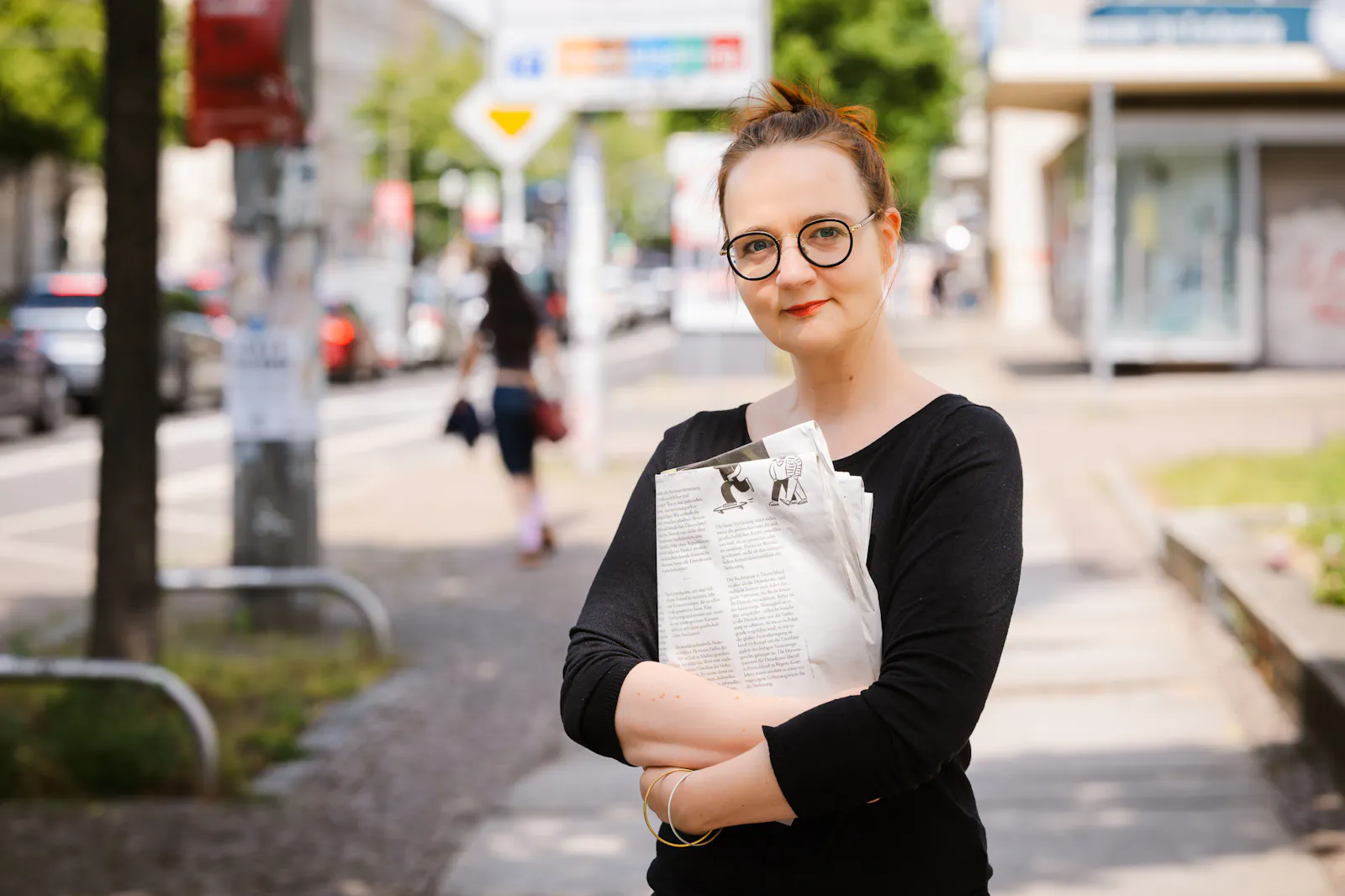 Insa van den Berg, Frau mit roten Haaren und Brille, hält zwischen verschränkten Armen eine Zeitung.