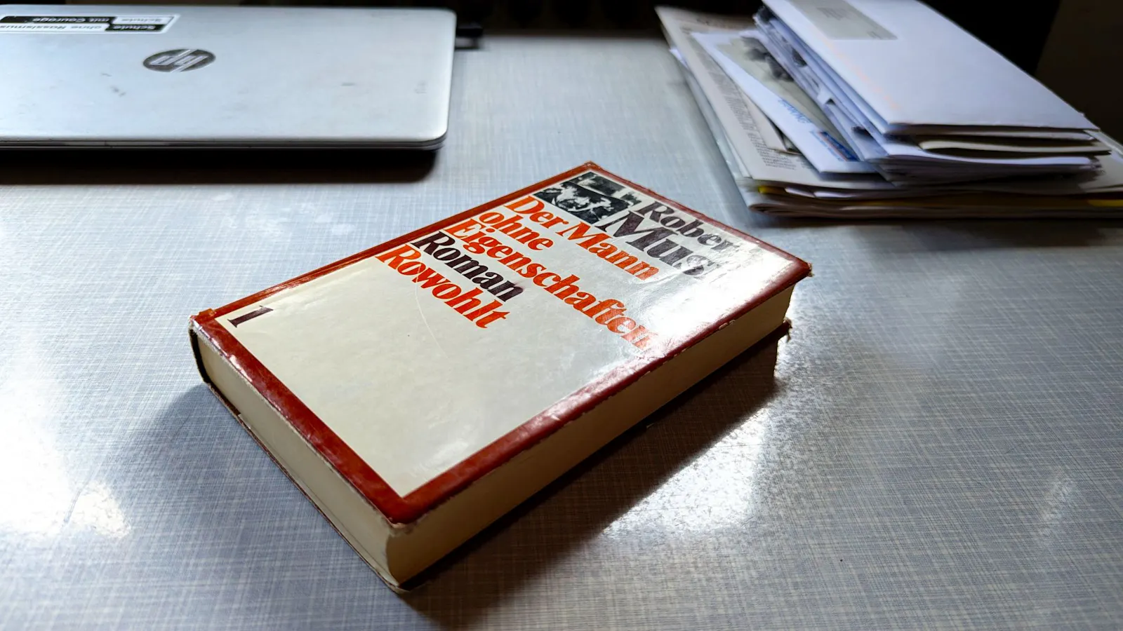 Ein Buch liegt auf einem Schreibtisch. Es handelt sich um den Roman 'Der Mann ohne Eigenschaften' von Robert Musil.