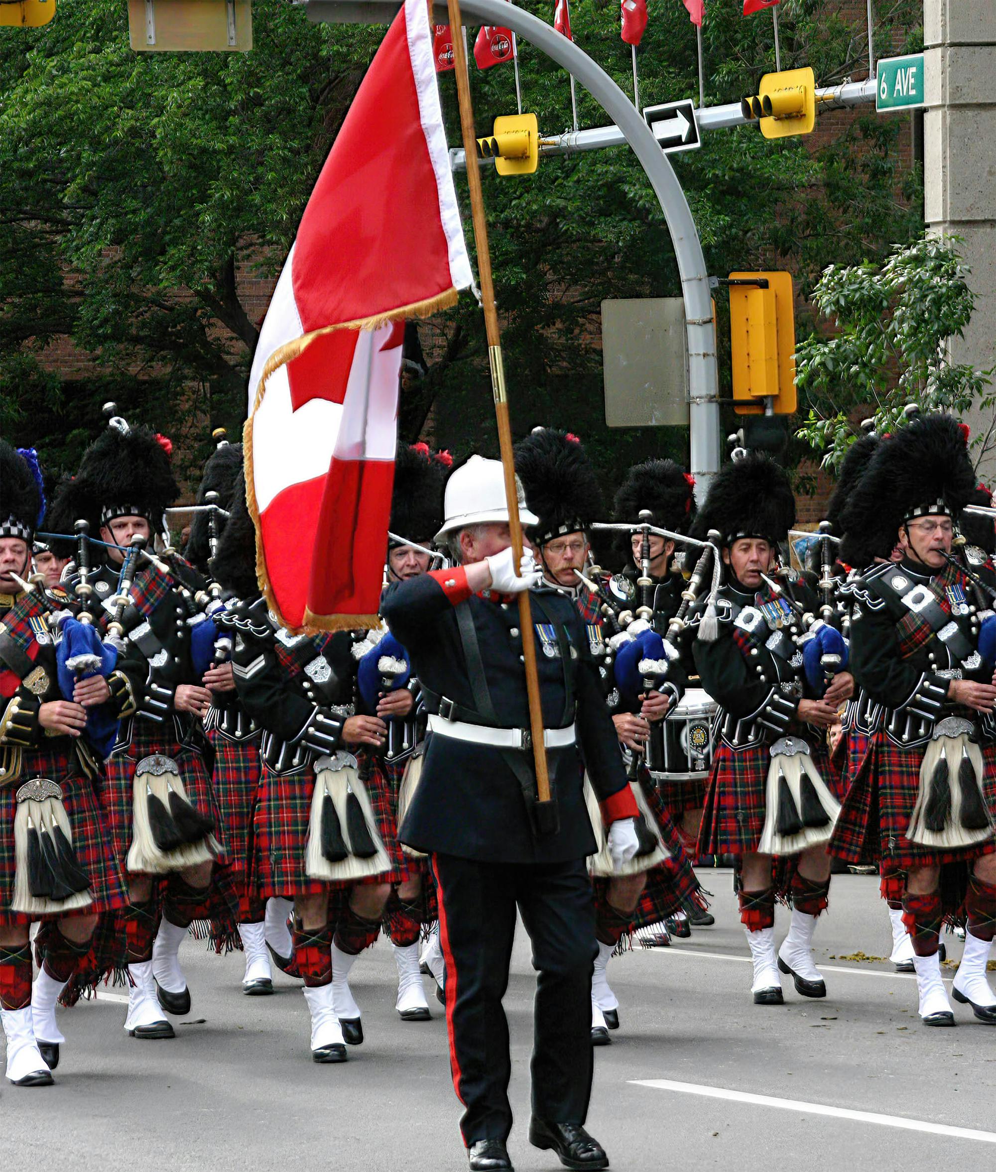 Marschierende Soldaten in Kilts mit Dudelsäcken hinter einer kanadischen Flagge.