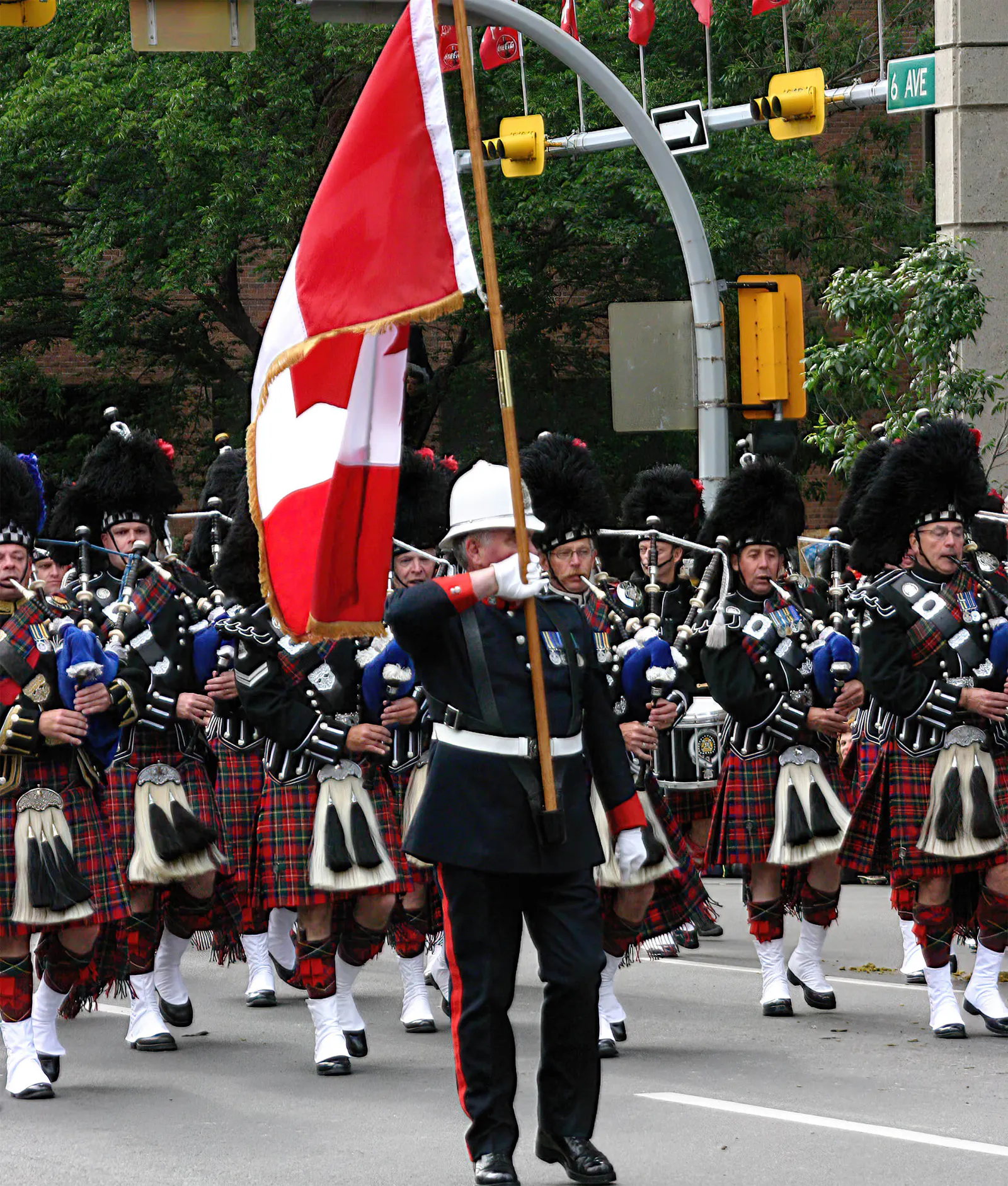 Marschierende Soldaten in Kilts mit Dudelsäcken hinter einer kanadischen Flagge.