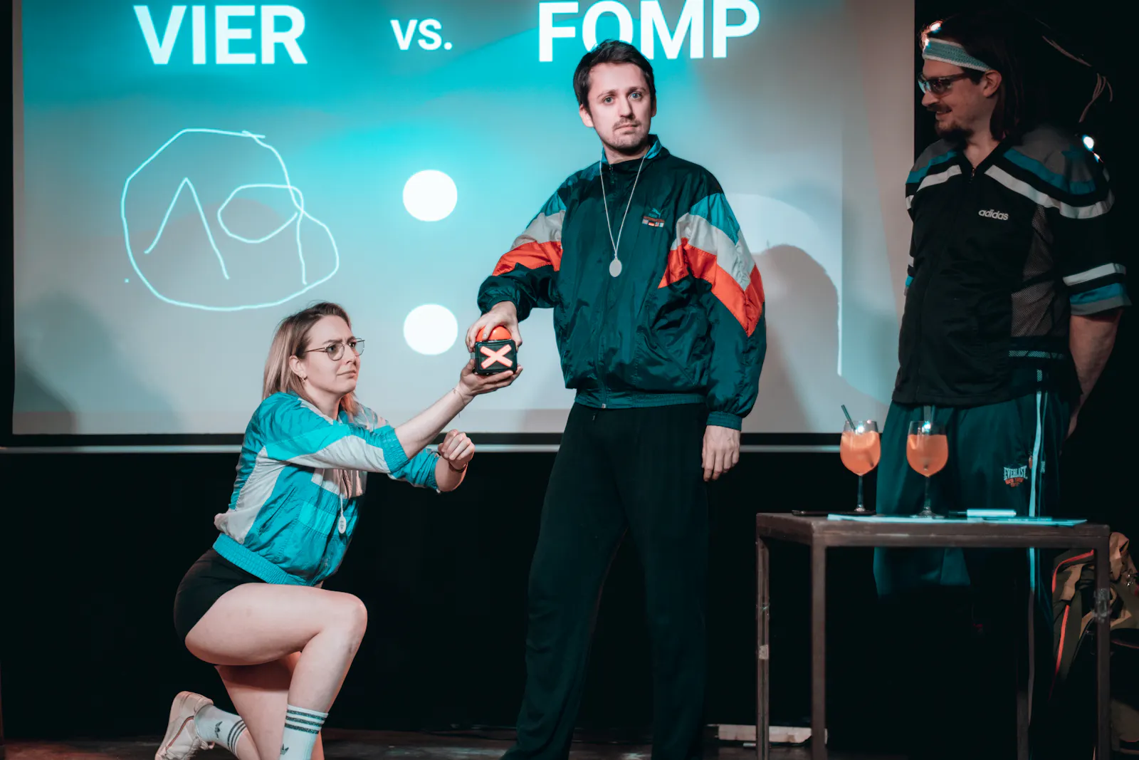 Fabian drückt auf einen Buzzer bei dem Event 4 vs. FOMP, Francesca Herr hält den Buzzer, Simon Tomaz steht daneben