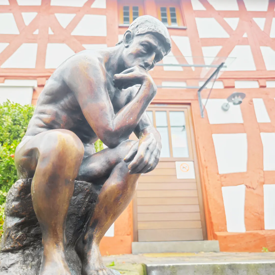 "Der Denker" von Rodin vor einem Fachwerkhaus