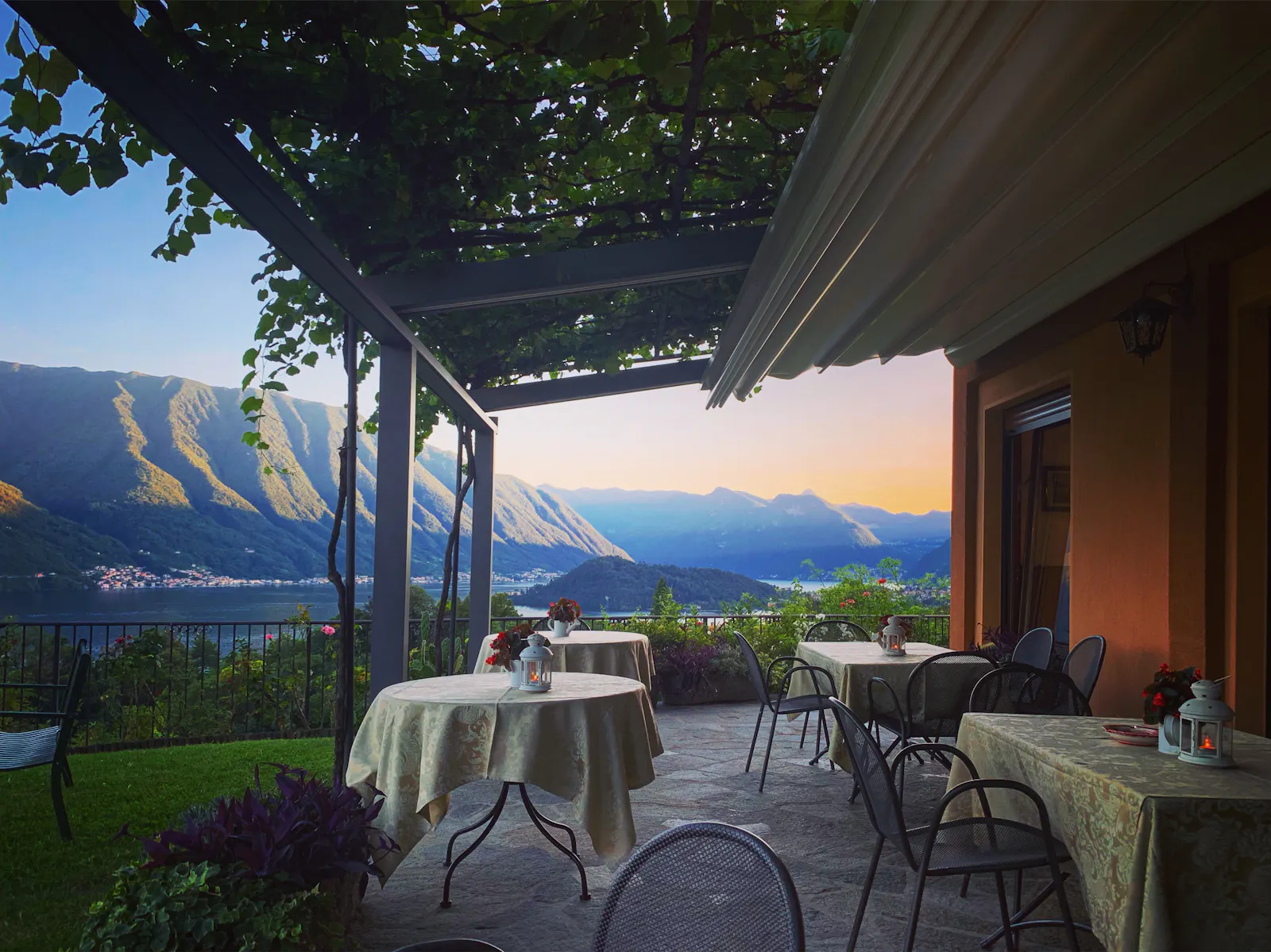 Tische auf einer einsamen Terrasse, noch nicht gedeckt, im Hintergrund der Comer See und die umliegenden begrünten Berge.