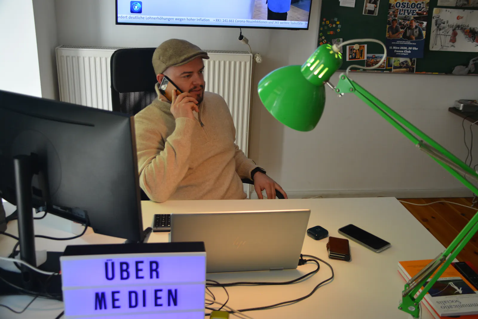 Frederik von Castell sitzt an seinem Schreibtisch in der Übermedien-Redaktion und telefoniert. Im Vordergrund: Übermedien-Schriftzug, Bildschirm und Schreibtischlampe.