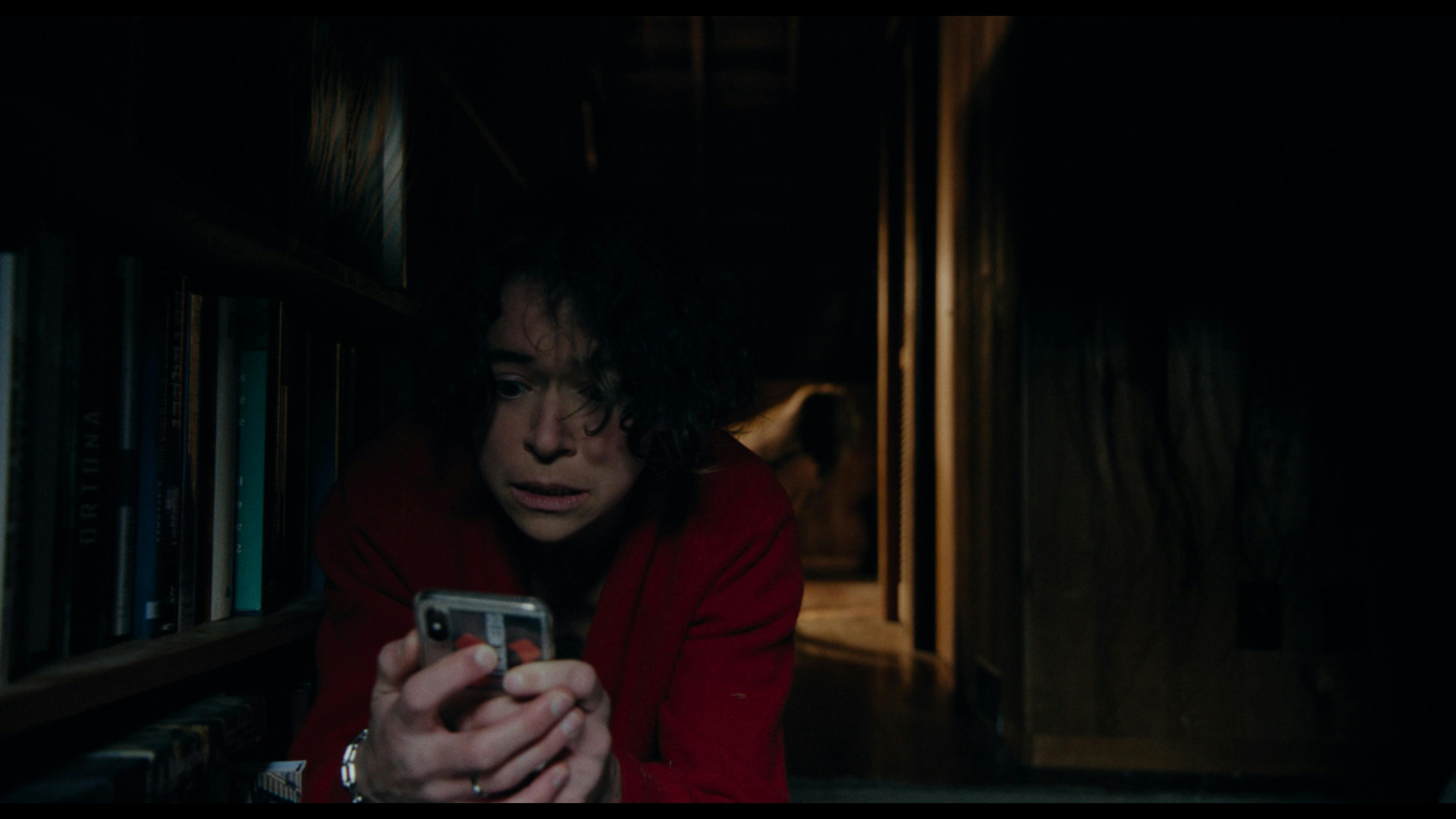 Liz mit Handy in der Hand auf dem Flurboden, hinter ihr eine unheimliche Gestalt