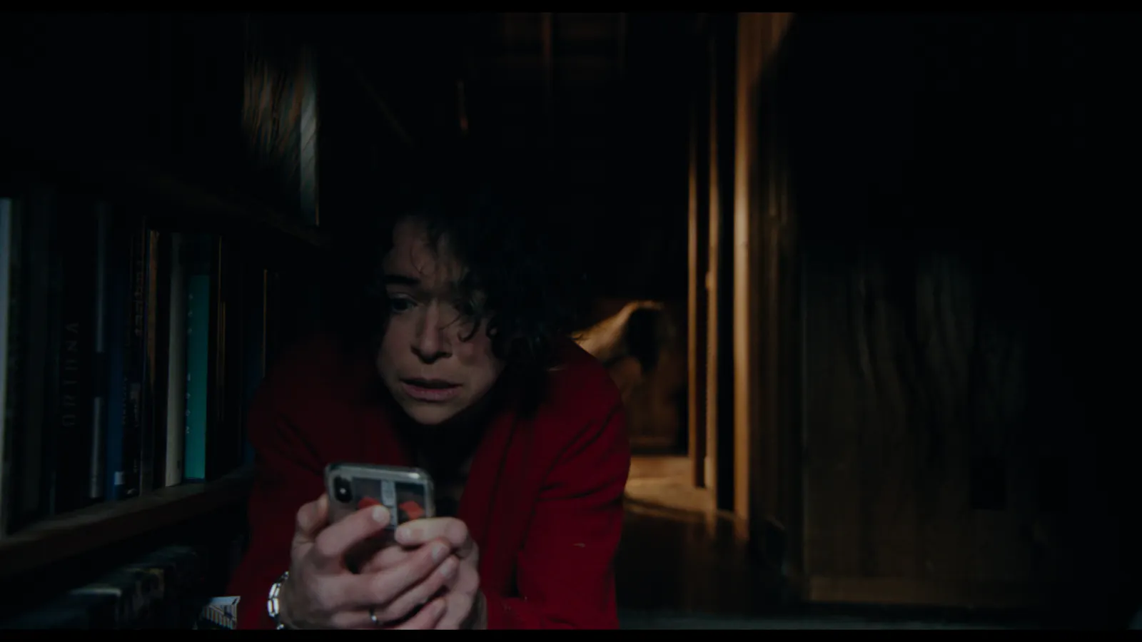 Liz mit Handy in der Hand auf dem Flurboden, hinter ihr eine unheimliche Gestalt