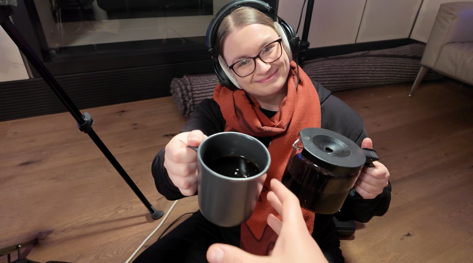 Carina reicht mit freundlichem Lächeln eine Tasse Kaffe.
