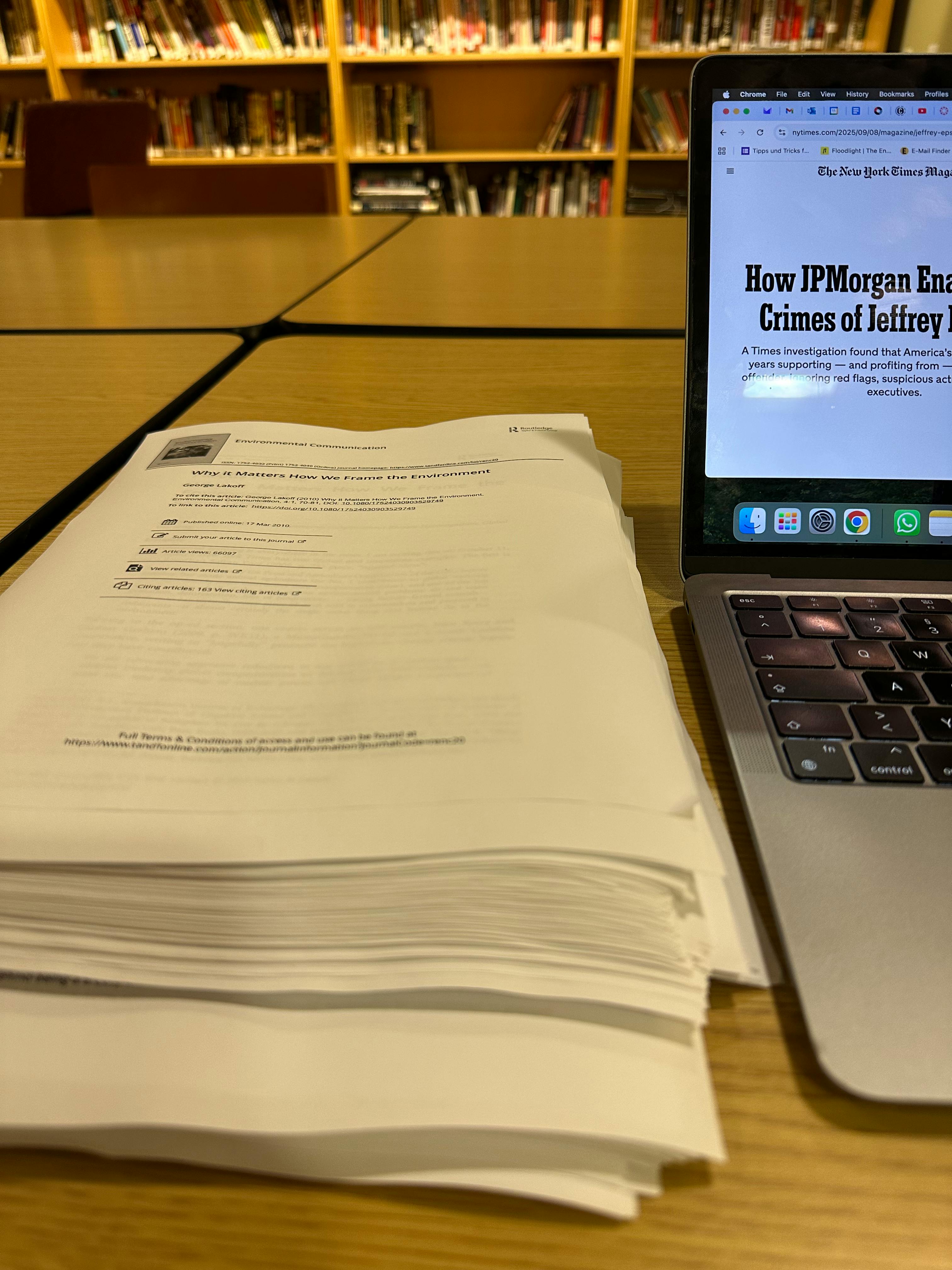Foto eines Papierstapels neben einem Laptop in einer Bibliothek.