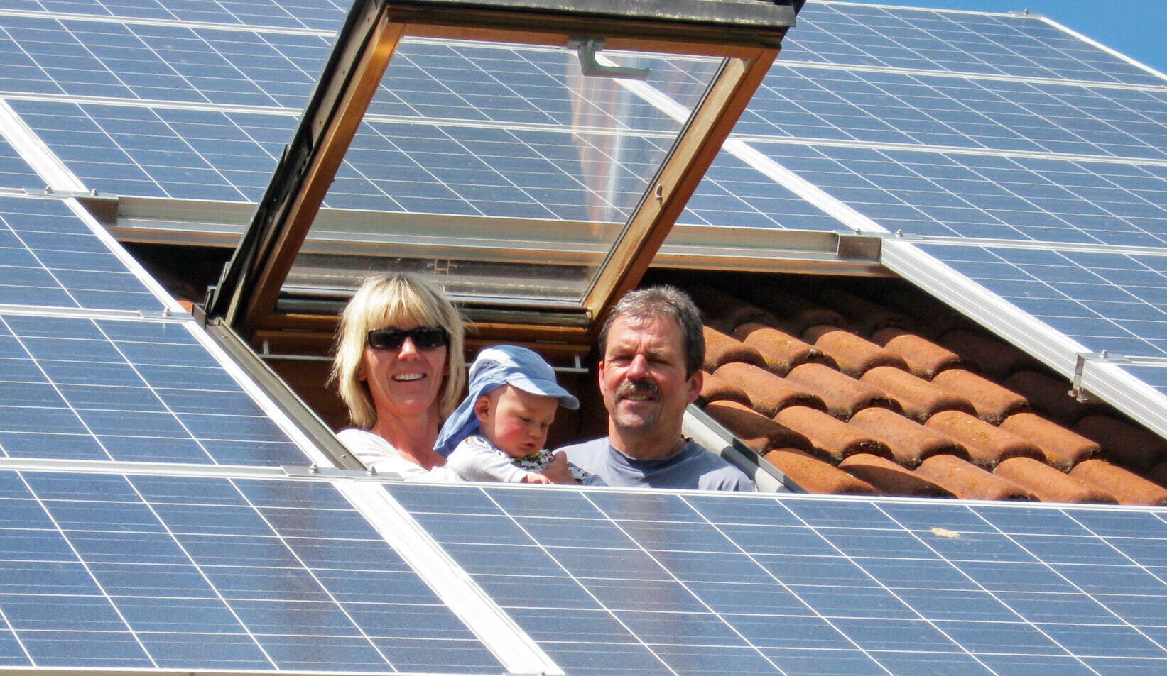 Familie schaut aus dem Dachfenster eines mit Photovoltaik bestückten Einfamilienhauses.