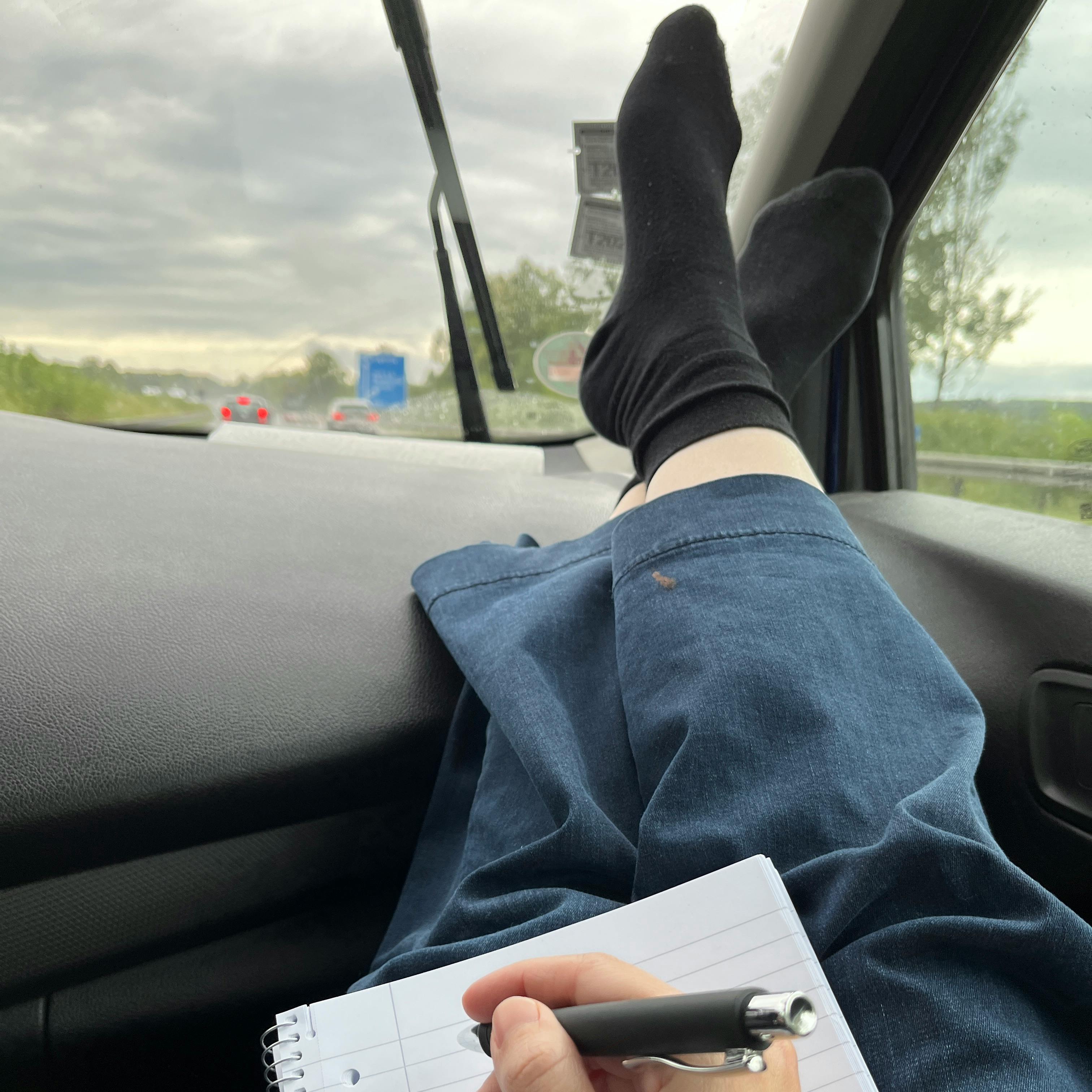 Miriam legt auf dem Beifahrersitz während der Fahrt die Beine hoch, auf ihrem Schoß liegt ein Block, sie hält einen Stift in der Hand.