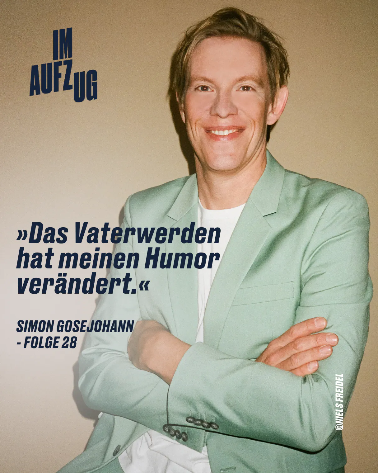 Das Vaterwerden hat meinen Humor verändert. - Simon Gosejohann Simon trägt ein hellgrünes Sakko und sitzt lächelnd vor einer gelben Wand.