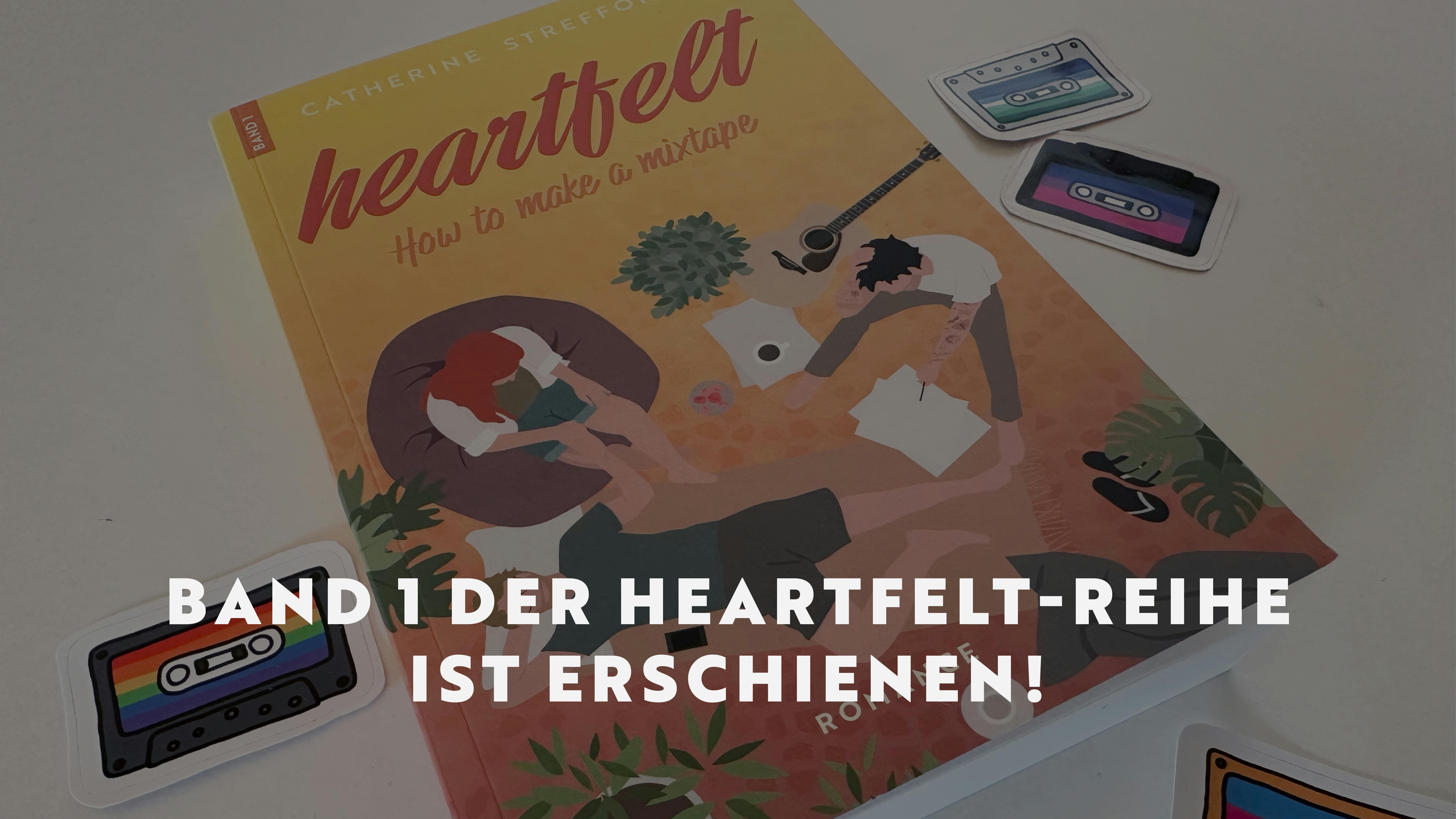 Das Taschenbuch von Heartfelt Band 1 liegt auf einem weißen Tisch, darum verteilt liegen Aufkleber von Musikkassetten in den Farben verschiedener Pride-Flaggen.