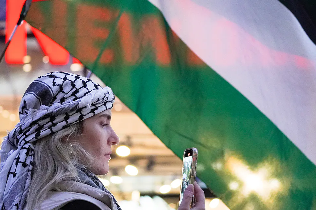 Demonstrantin mit Kufiya vor einer palästinensischen Flagge